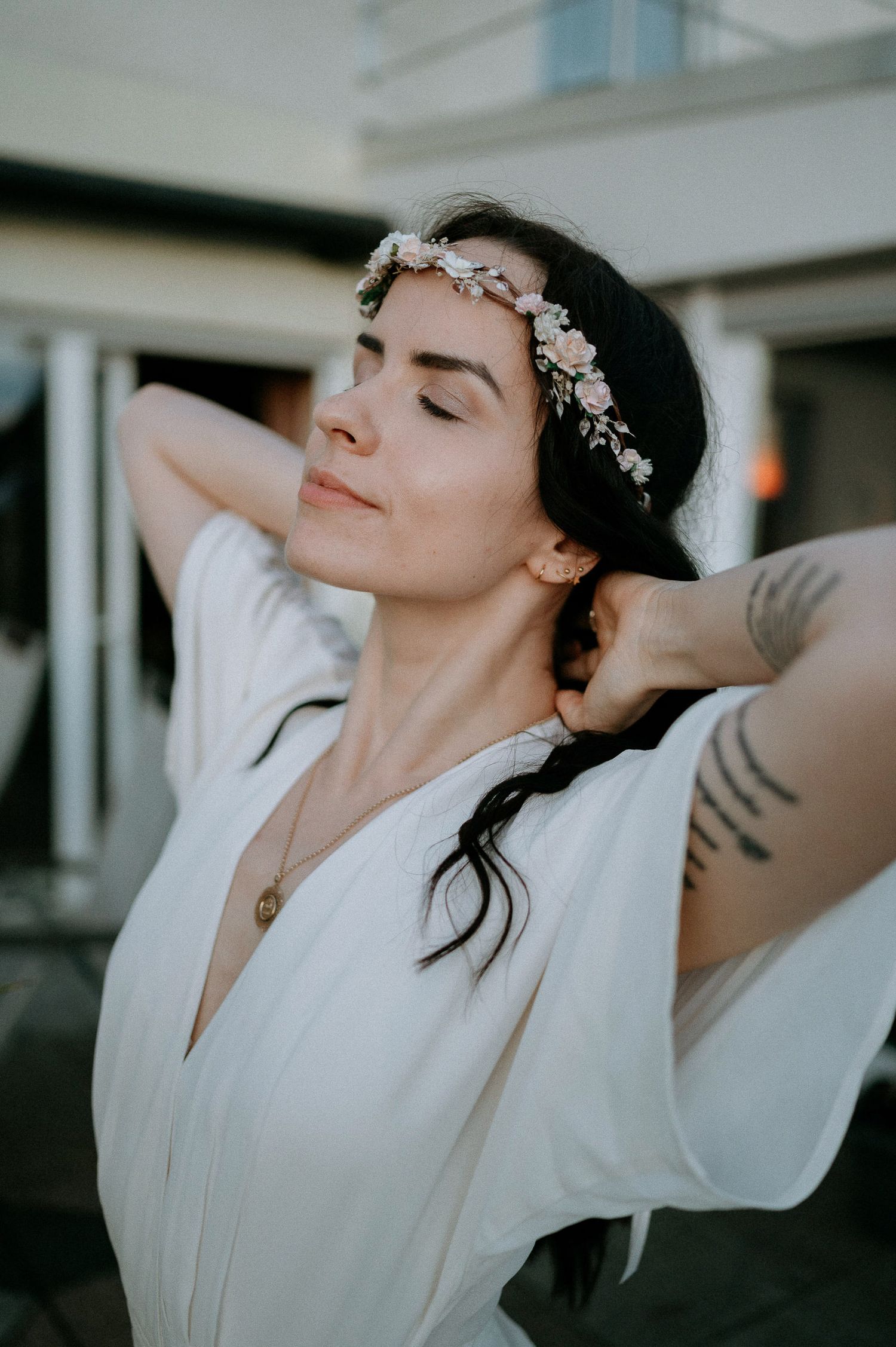 Person in white dress wearing floral headpiece poses with eyes closed in natural light.