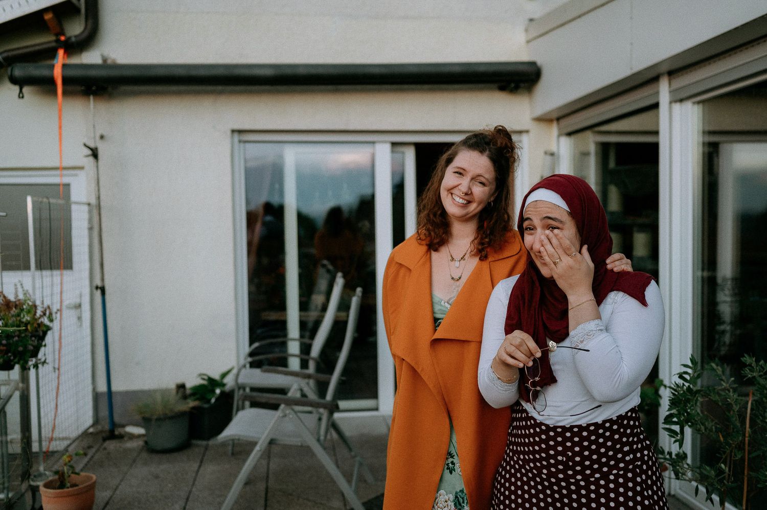 A couple shares a joyful moment on a balcony with white buildings in the background.