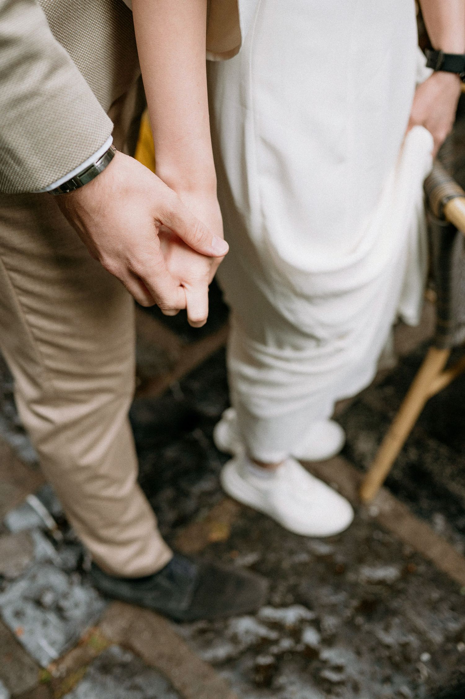 Close-up of two people holding hands while wearing light-colored formal attire.