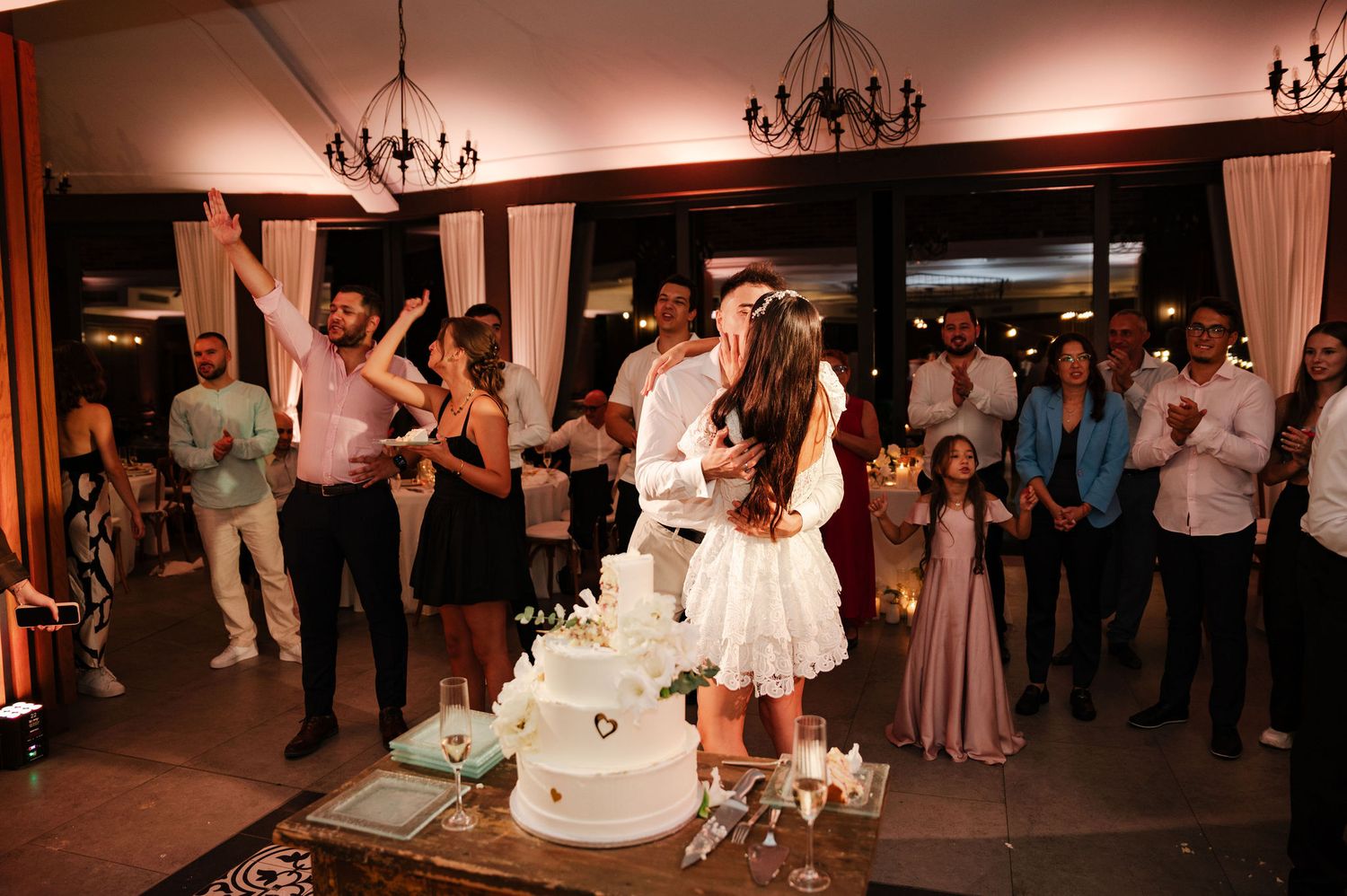 Wedding reception guests dancing and celebrating under elegant chandeliers at an indoor venue.