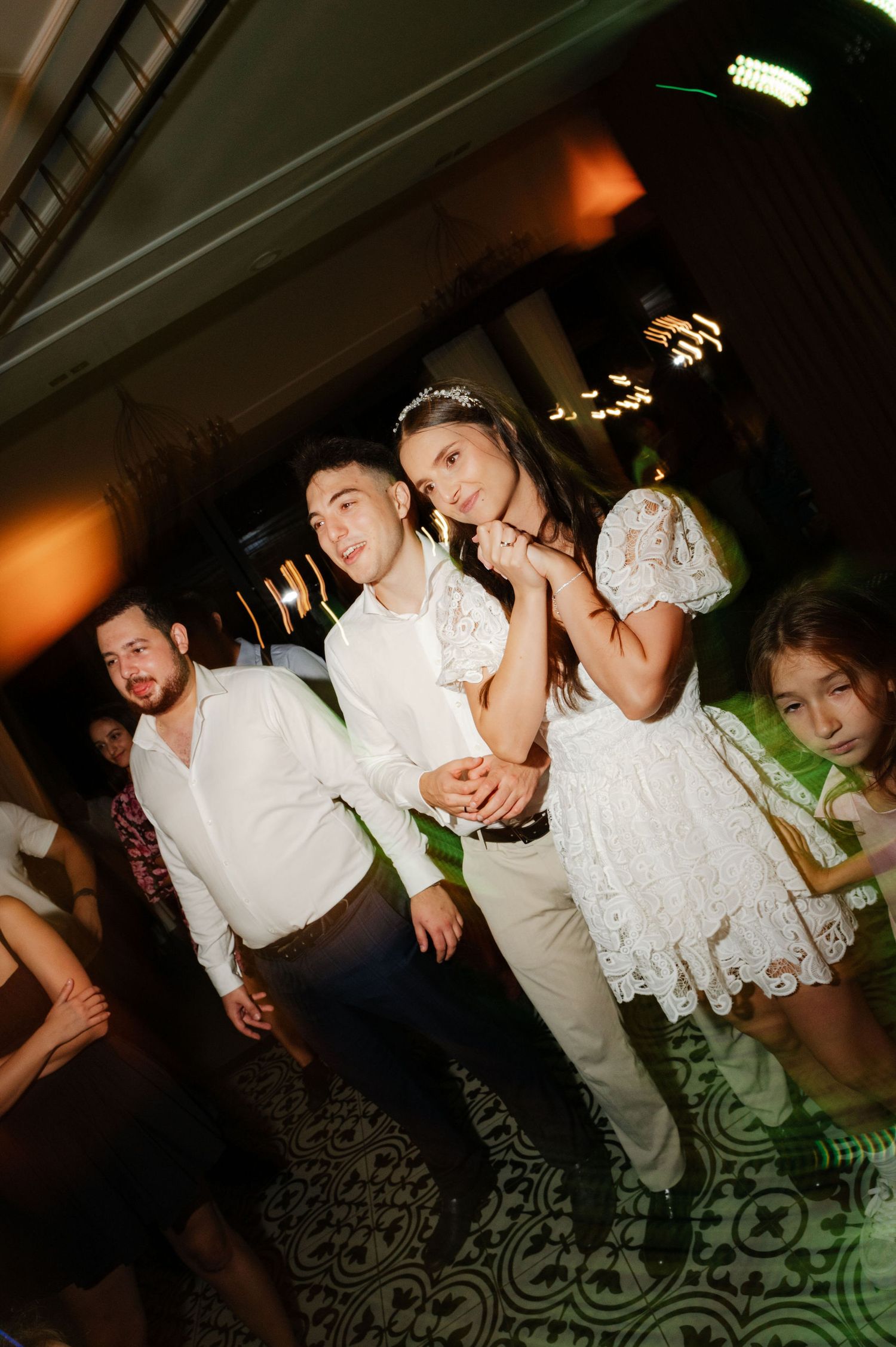 Guests dance and celebrate on a patterned floor under moody lighting at an indoor event.