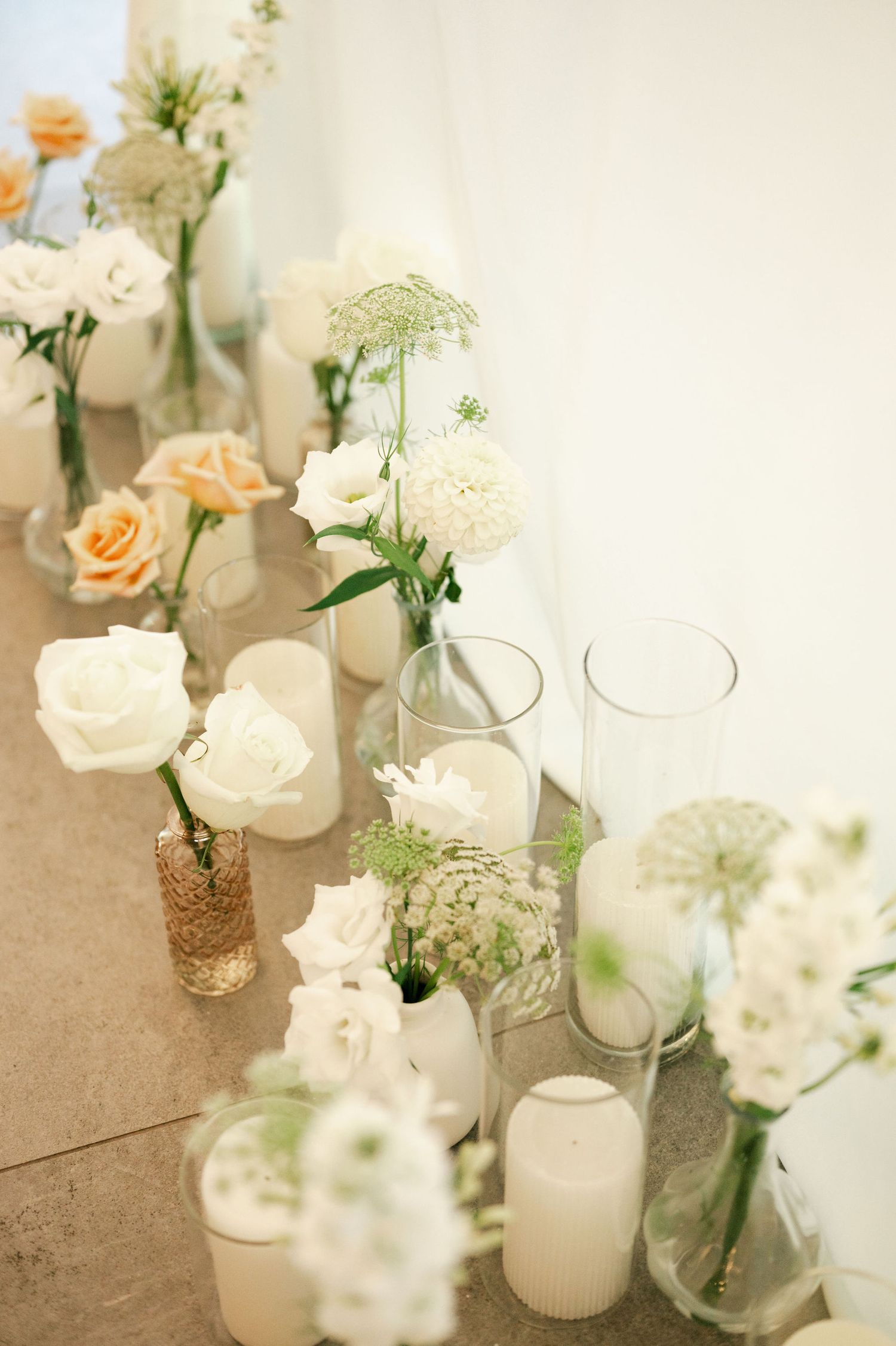 Romantic table decor with peach roses and white flowers in glass vases with gold accents.
