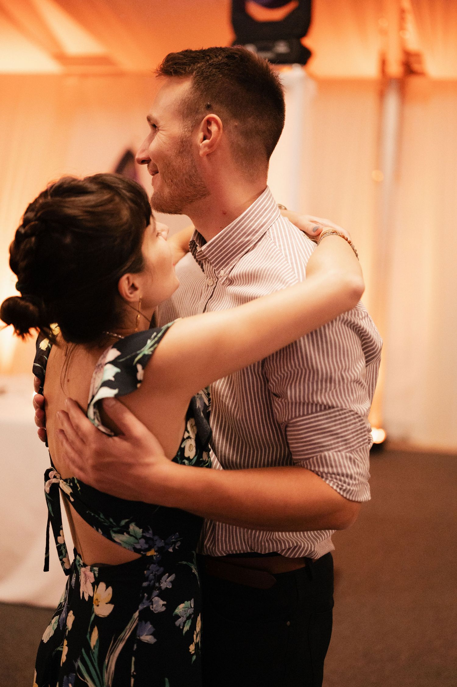 A couple dances together in an intimate embrace with warm orange lighting creating a romantic atmosphere.