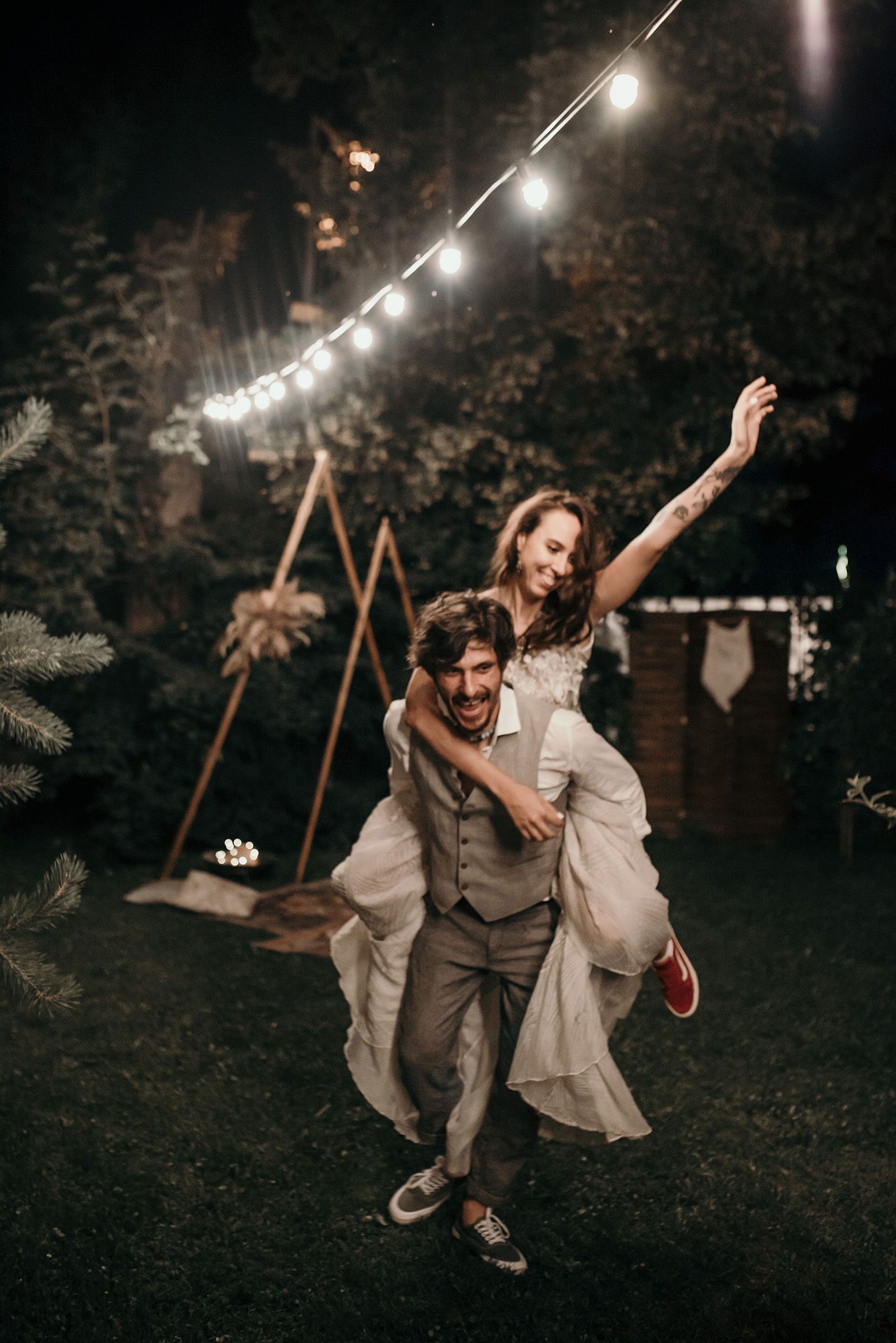 A couple dances joyfully under string lights at a nighttime outdoor celebration, creating a romantic atmosphere.
