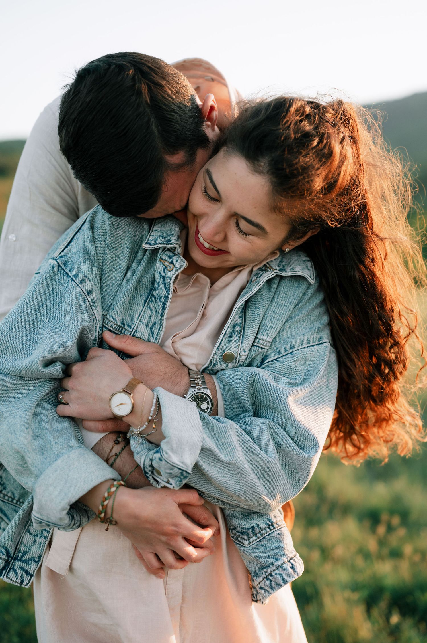 A romantic couple in denim embraces outdoors during golden hour while sharing intimate moments in a natural setting.