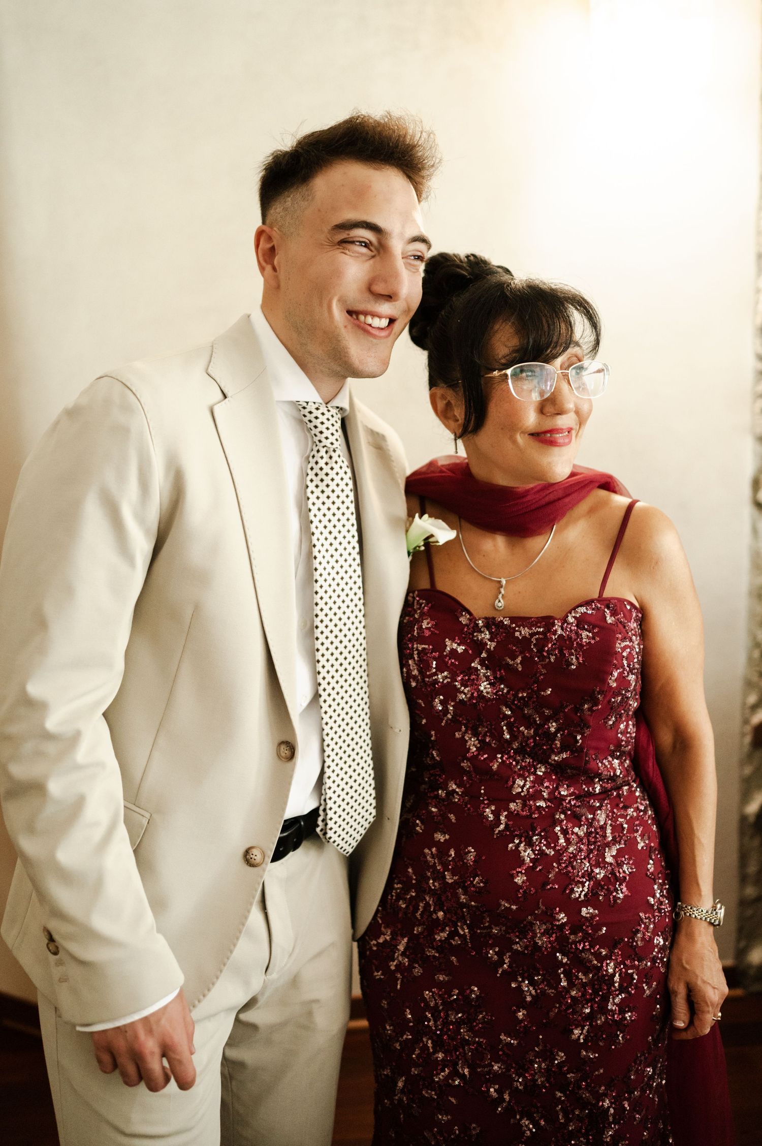 A couple in formal attire, with a white suit and burgundy sequined dress, share joyful moments together.