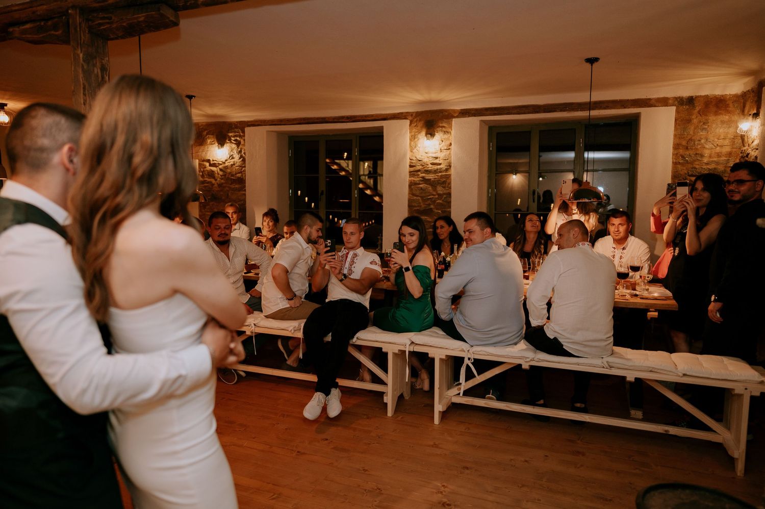 Couple sharing a romantic dance moment surrounded by guests in a beautifully lit reception hall.