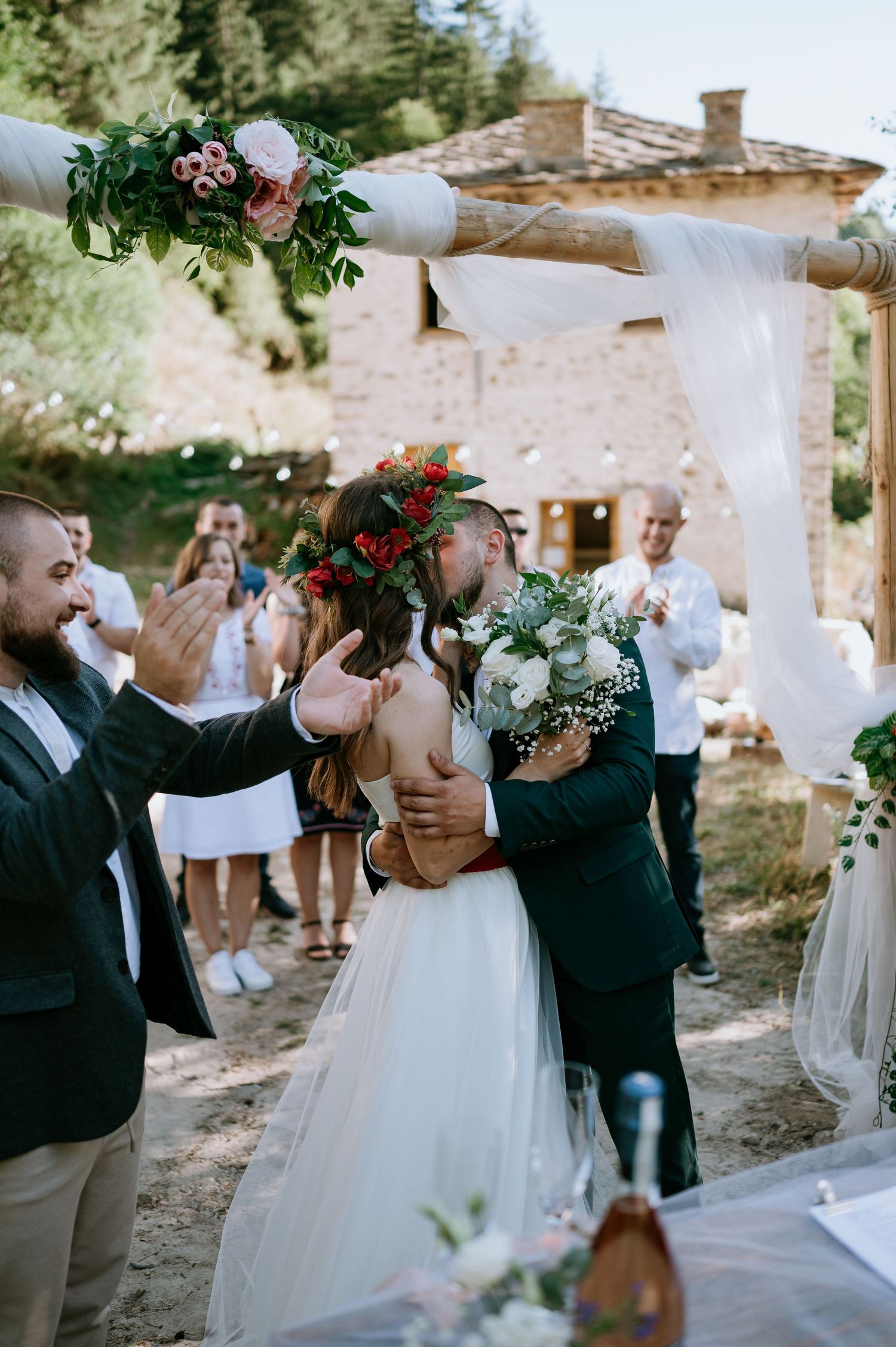 Festive outdoor wedding scene with white curtains and natural decor against stone building.
