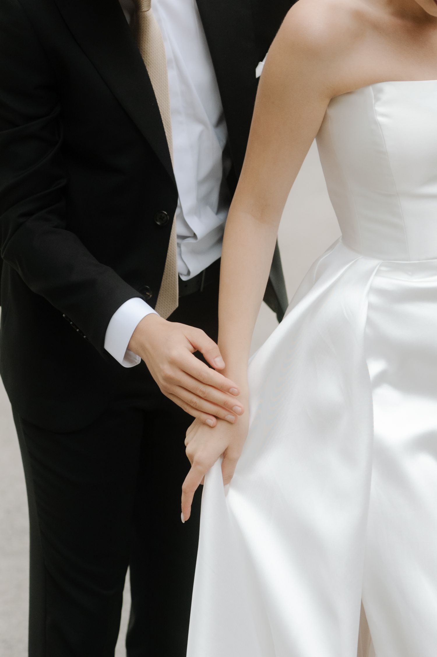 Close-up shot of a couple in wedding attire, showing hands touching, with black suit and white dress details.