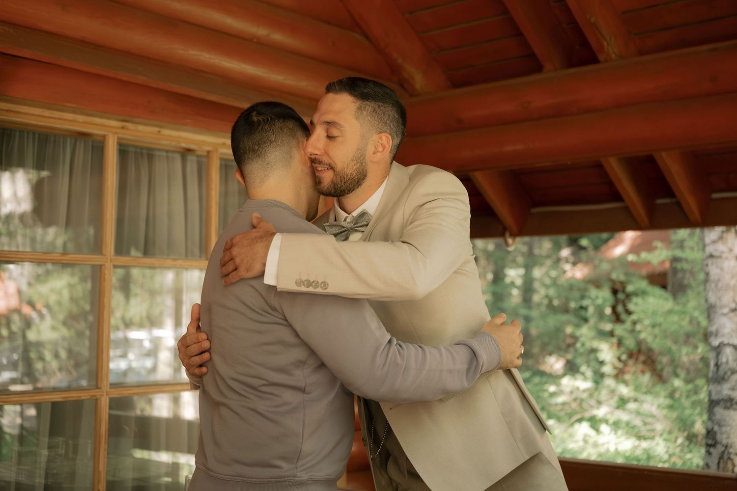 Two men in suits sharing a warm embrace at an elegant wooden venue during a wedding celebration.