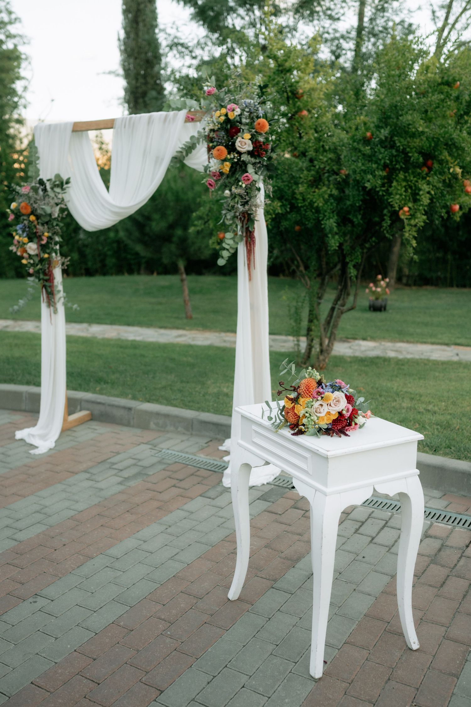 White wooden chairs decorated with floral arrangements and flowing white fabric create an elegant outdoor ceremony setup.