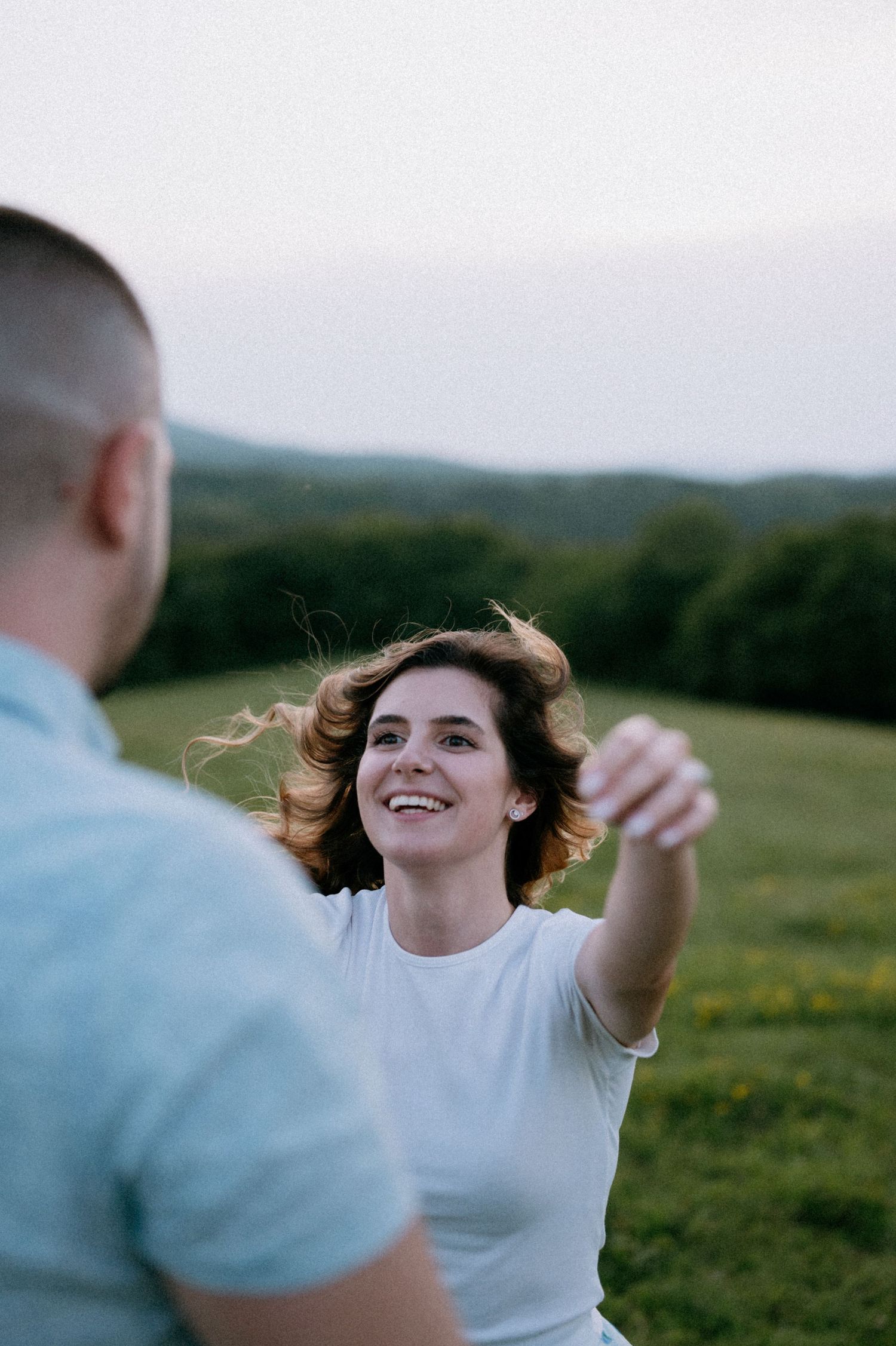 Person in white twirling joyfully in an open meadow with mountains in background.