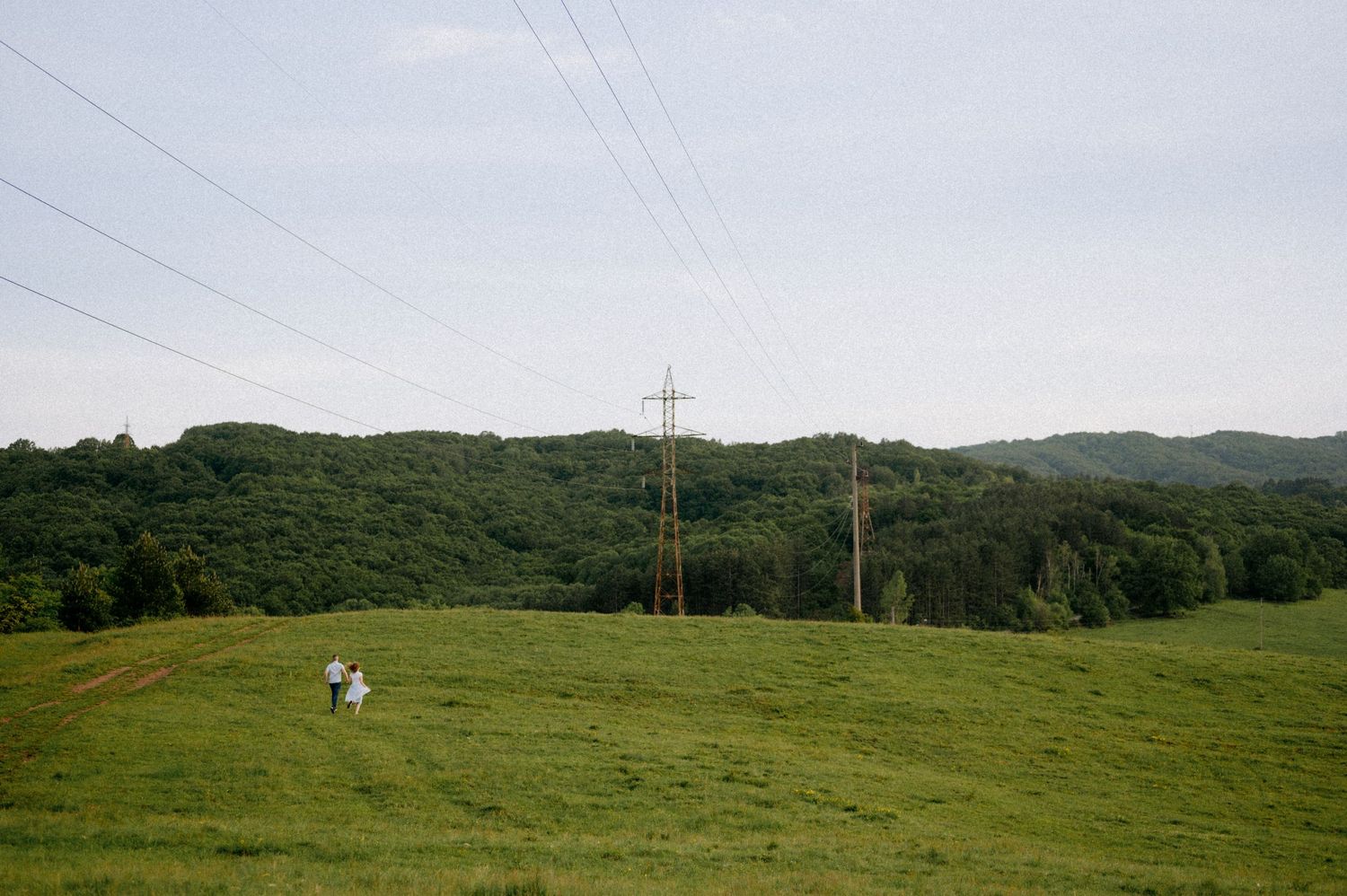 Scenic hilltop view showing power transmission lines spanning across verdant countryside.