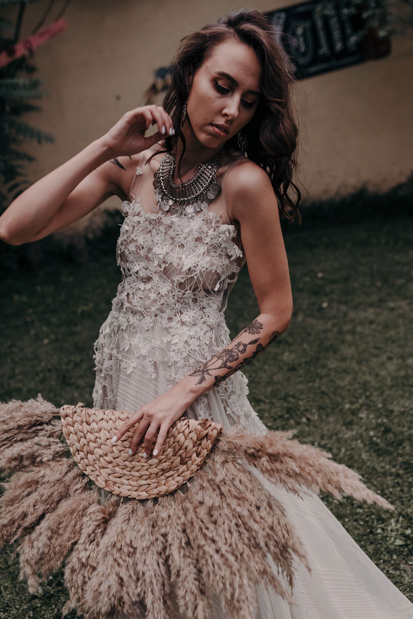 A model in an ornate white dress with feathered details poses gracefully in a garden setting.