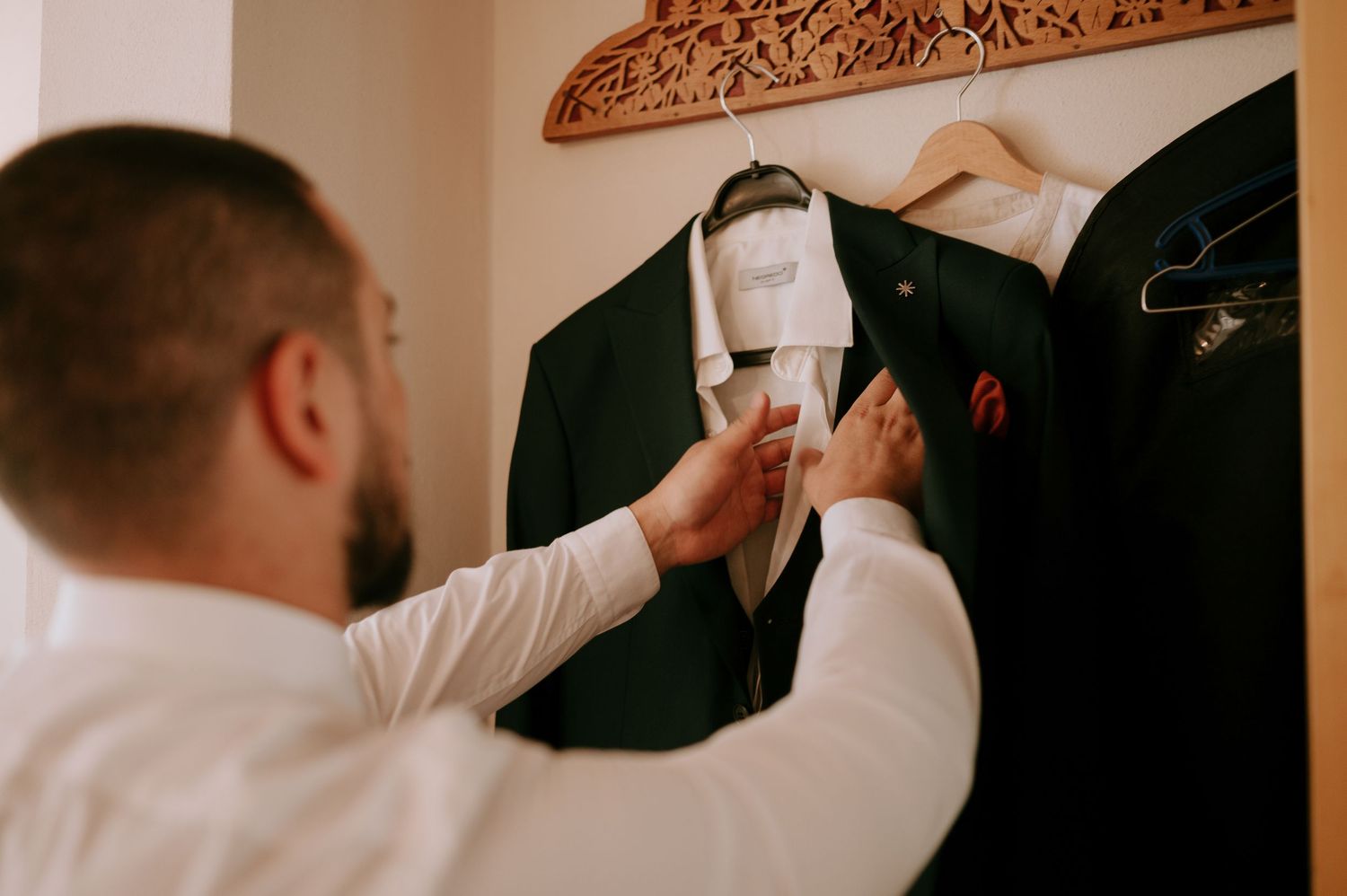 Hand adjusting formal suit jacket on ornate wooden hanger.