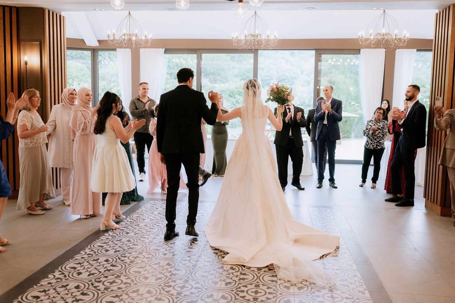 Wedding celebration in a spacious reception hall with large windows and elegant chandeliers.