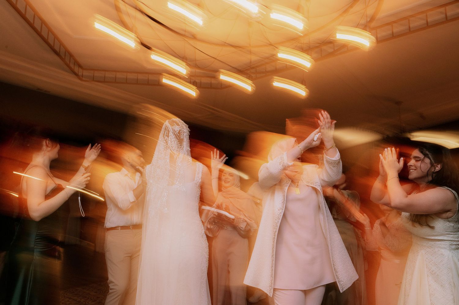 Motion-blurred dancers celebrate at a wedding reception under ambient lighting.