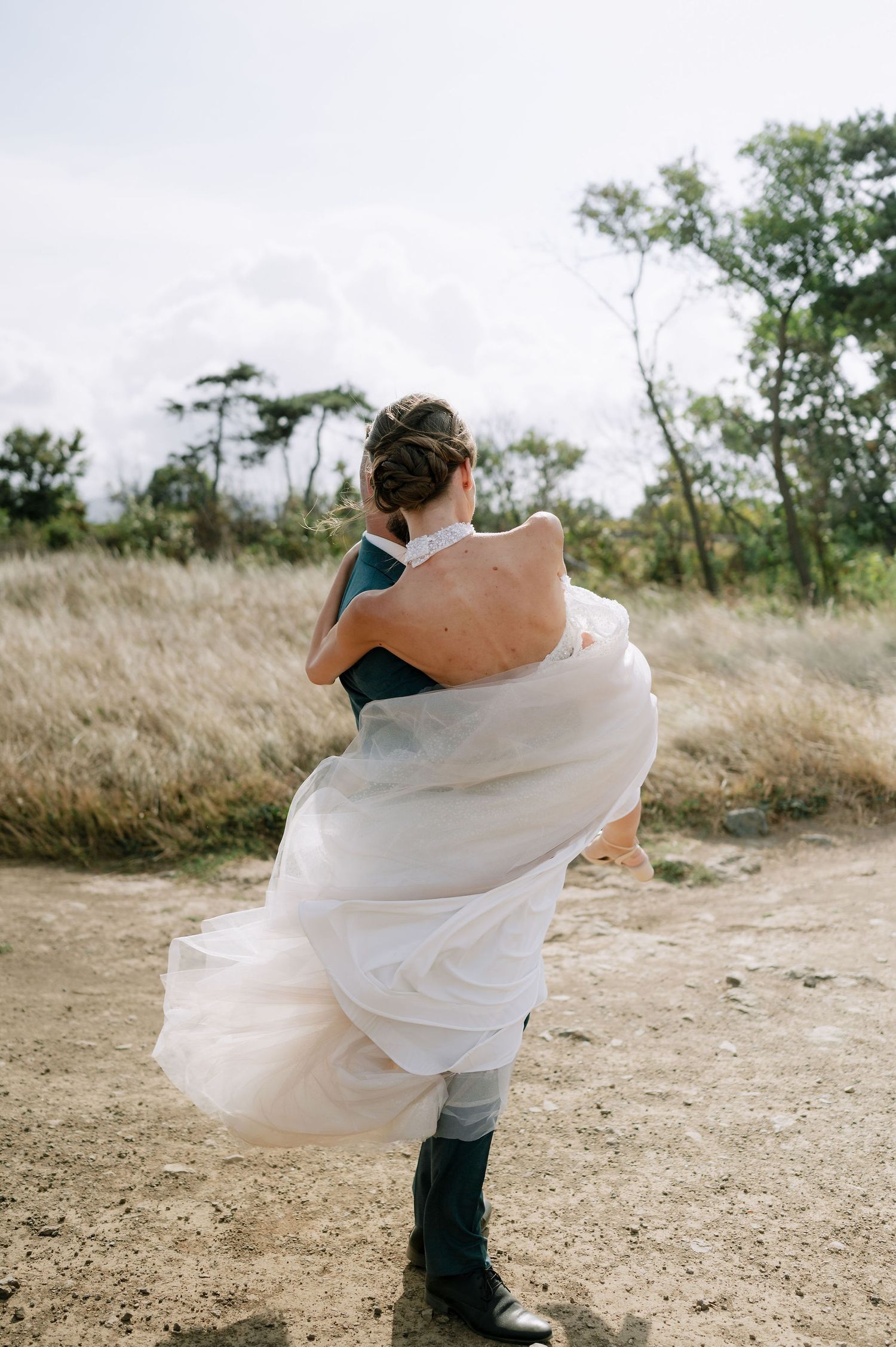Couple embraces in dramatic pose on natural path during wedding photoshoot.