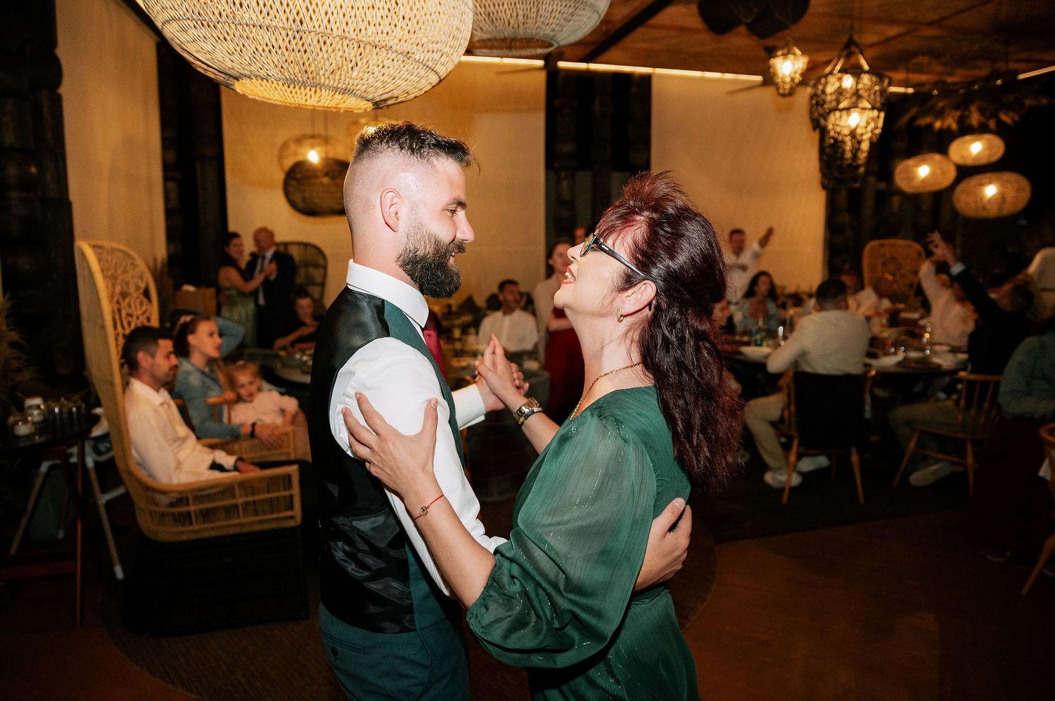 Wedding party dancing energetically at evening reception under warm lighting.