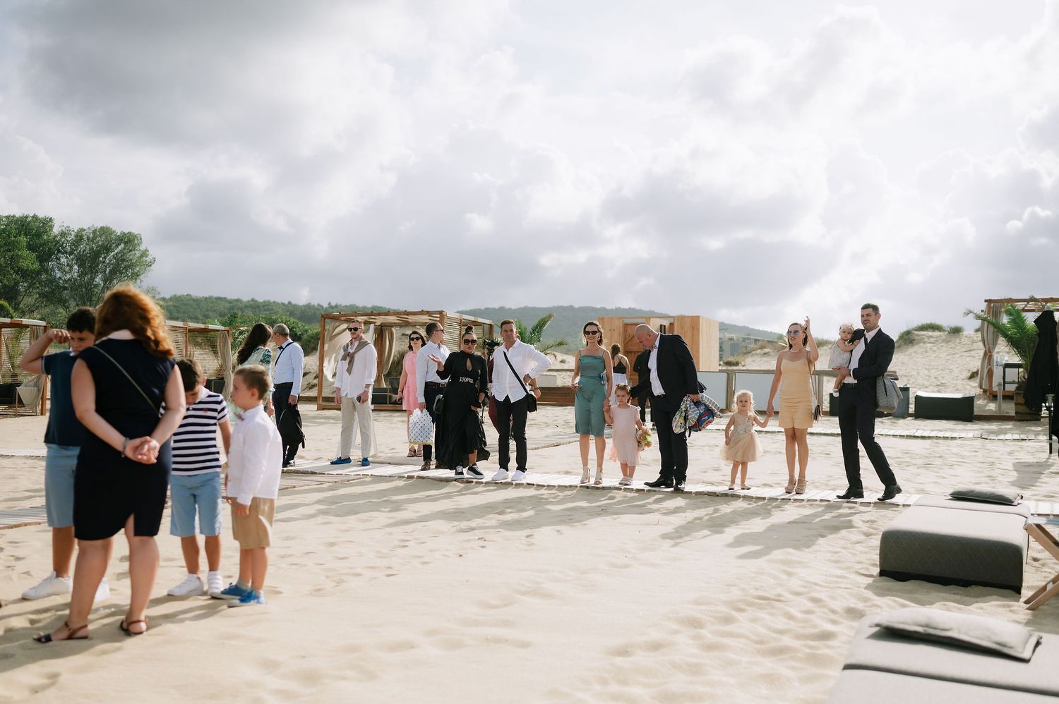 Wedding guests gather on a sunny beach under cloudy skies.