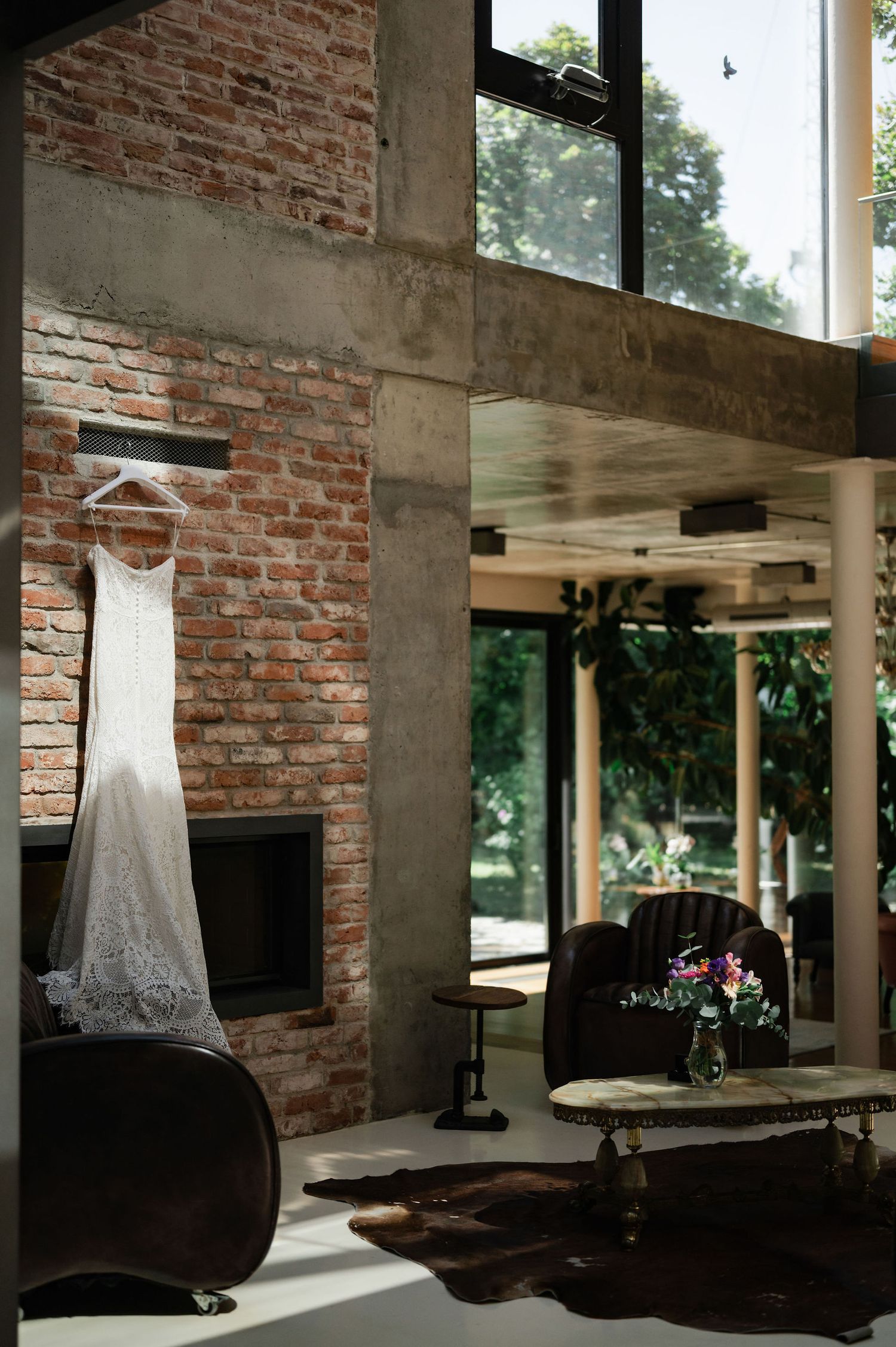 Sunlit wedding dress hanging in contemporary venue with exposed brick and concrete pillars.