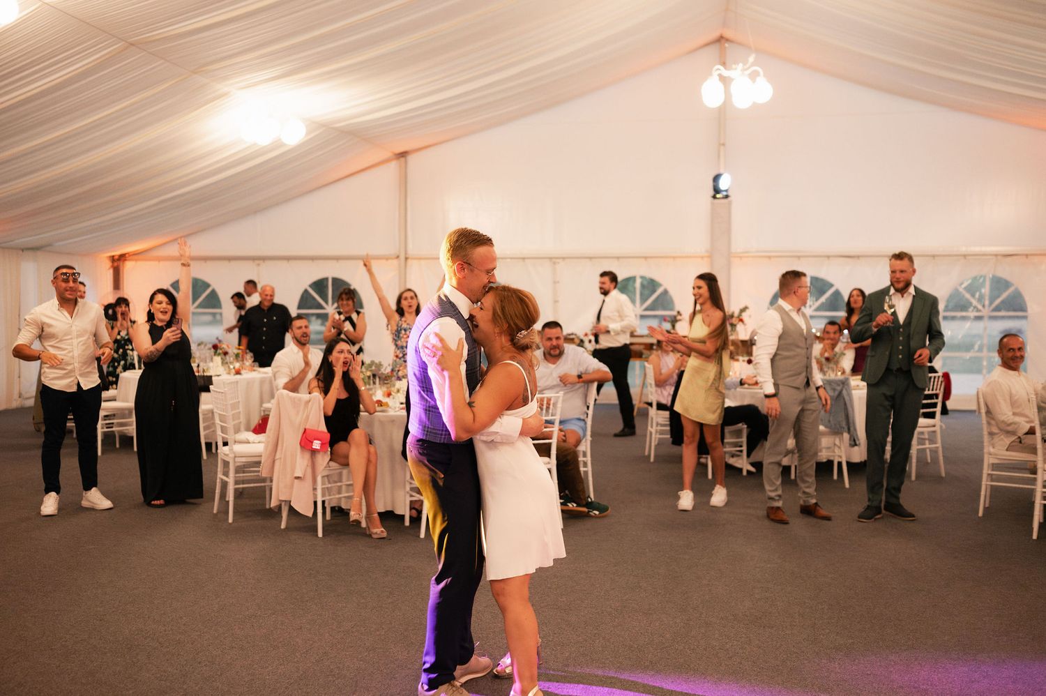Wedding reception in a white tent with guests dancing on the dance floor.