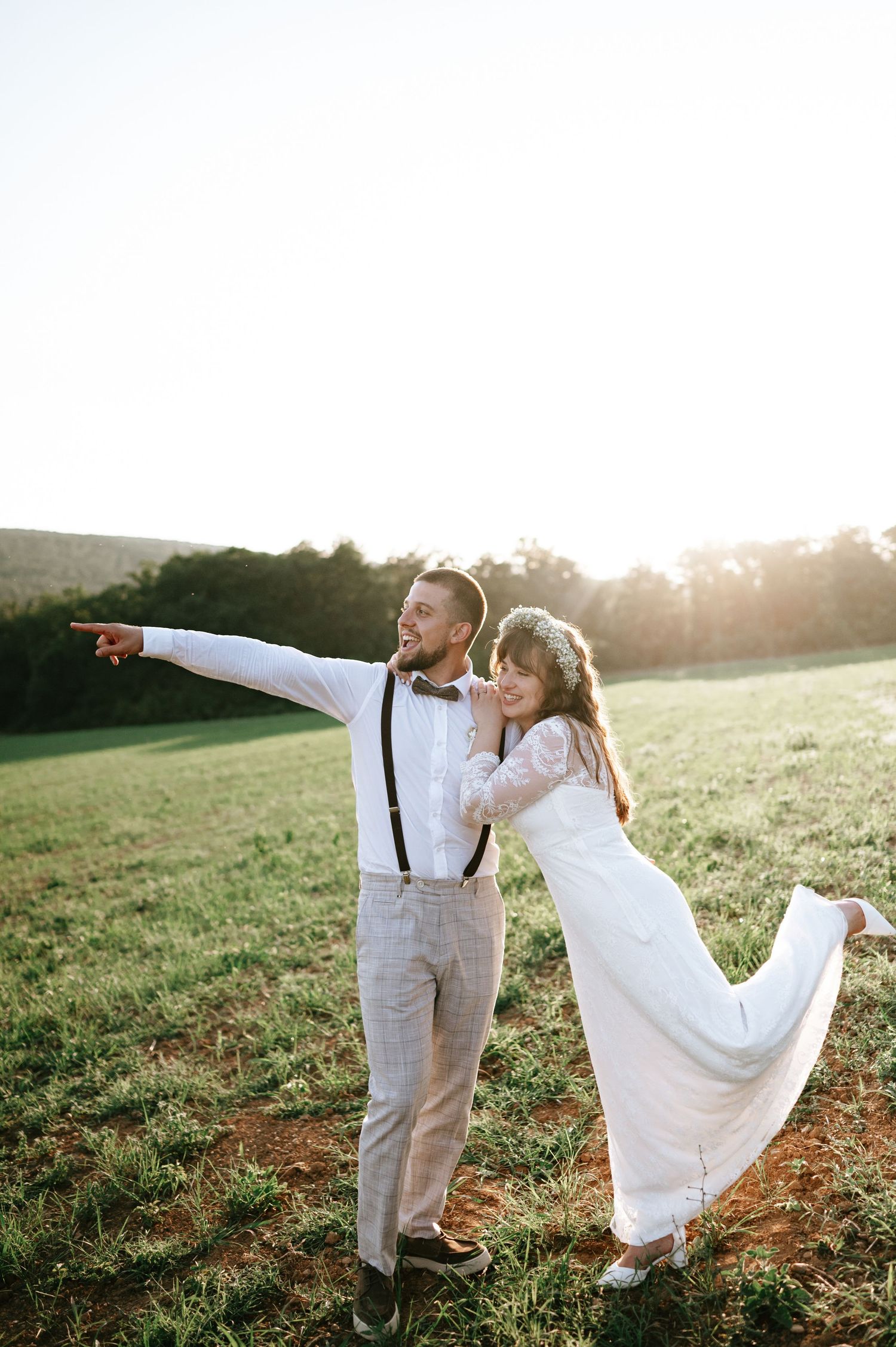 Bride and groom dance joyfully in a field during sunset.