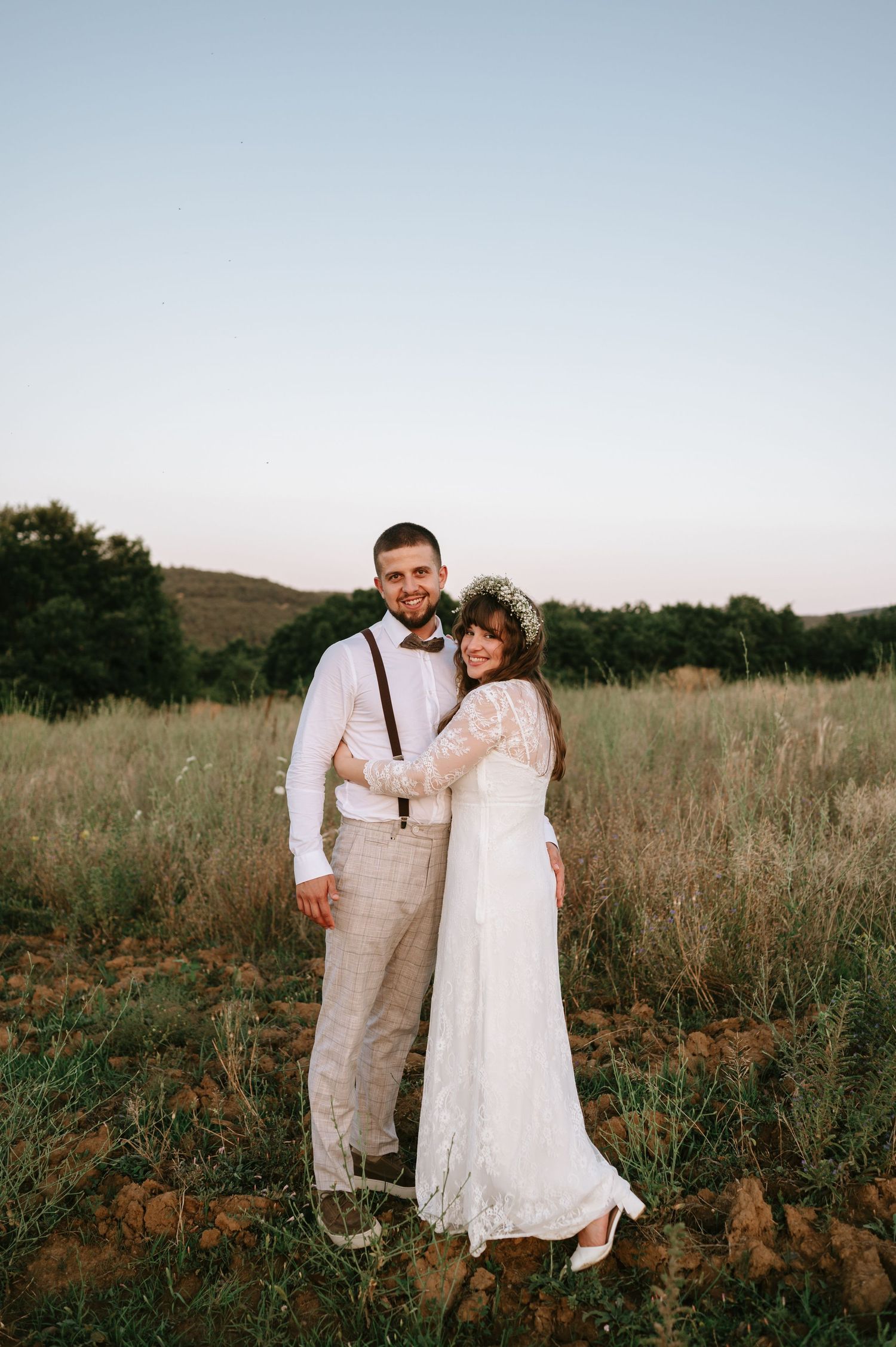 A couple poses together in a field at dusk with mountains visible in the background.