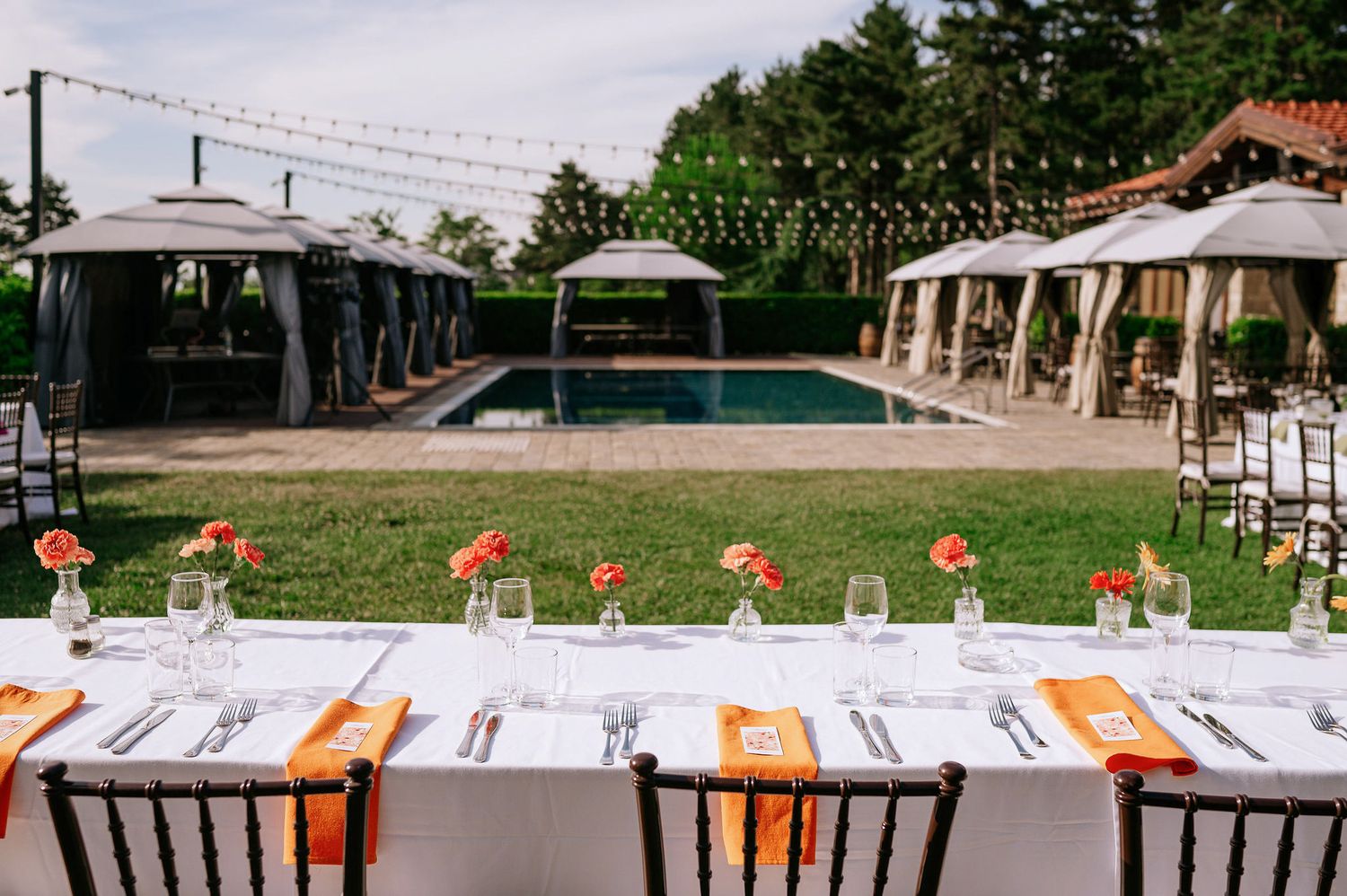 Outdoor reception setup with orange accents and string lights creating a festive atmosphere.