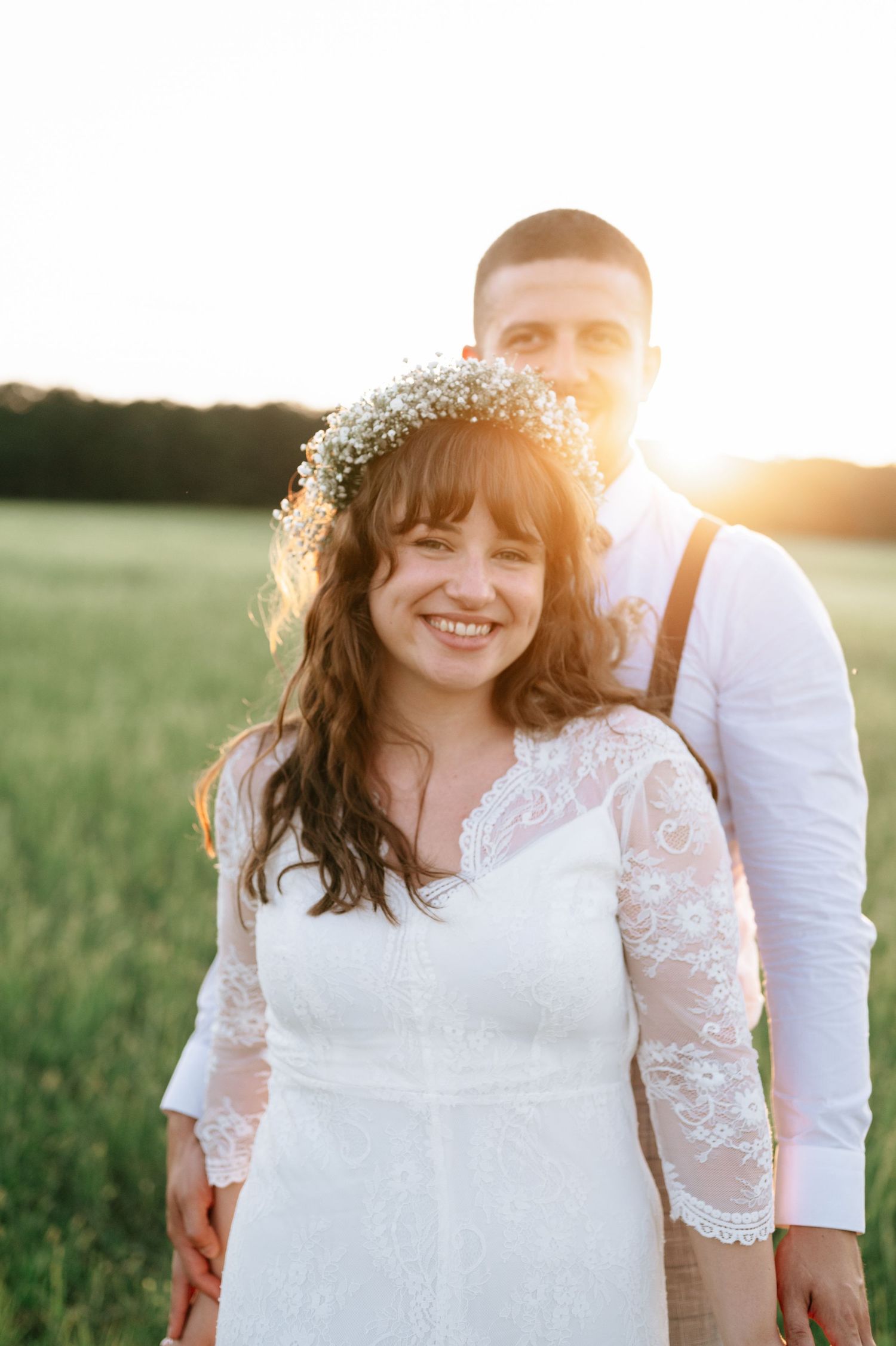 A couple poses in a sunlit field during their wedding photoshoot at golden hour.