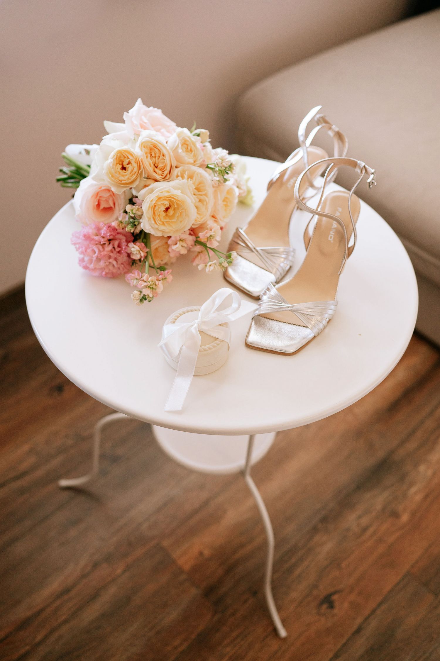 Wedding accessories including peach roses and white bridal shoes displayed on round white table.
