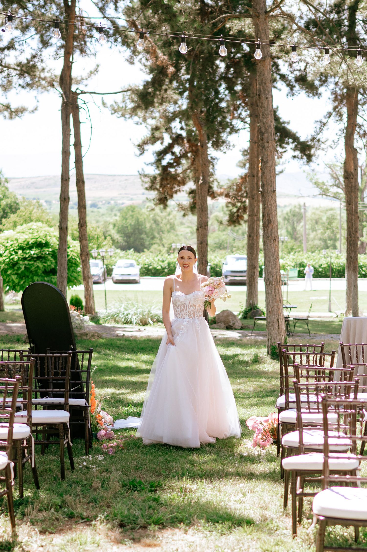 Outdoor wedding ceremony site with wooden chairs arranged in rows under towering pine trees.