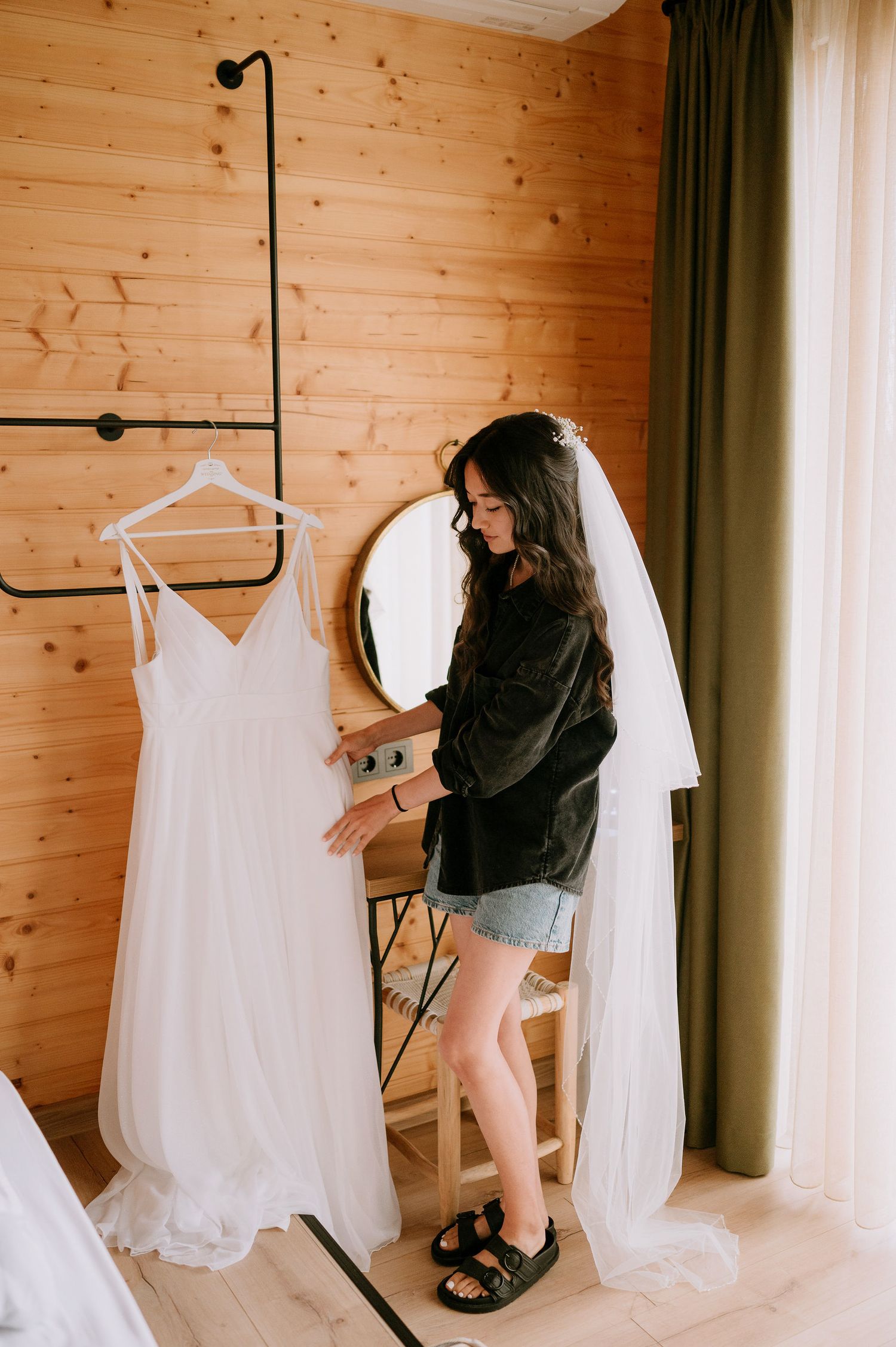 Wedding dresses and veils displayed on hangers in rustic wooden room.