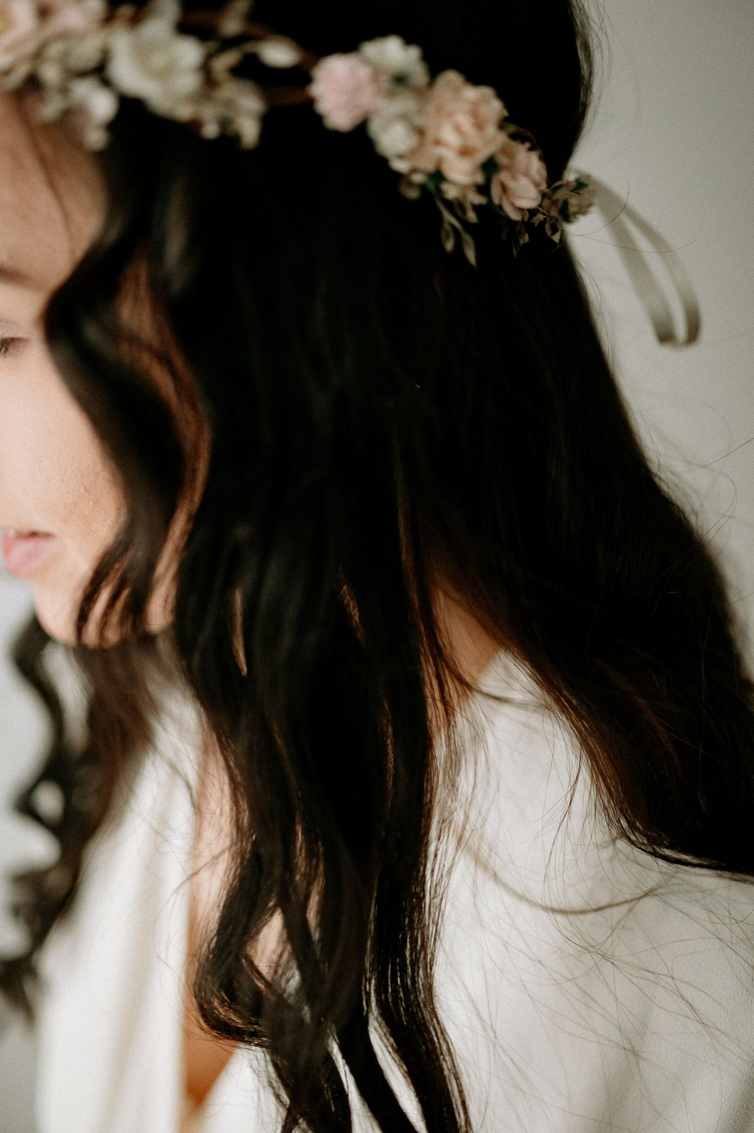 Artistic portrait showing dark wavy hair adorned with delicate pink flowers against a light background.