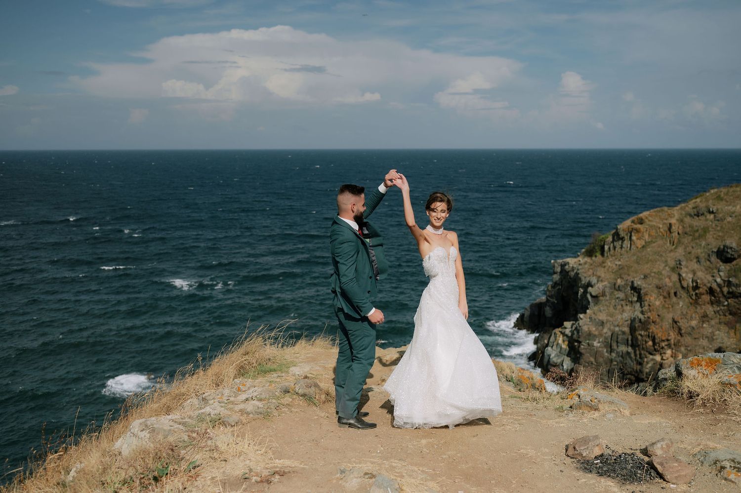 A couple shares an intimate moment on a scenic coastal cliff with blue ocean waters in the background.