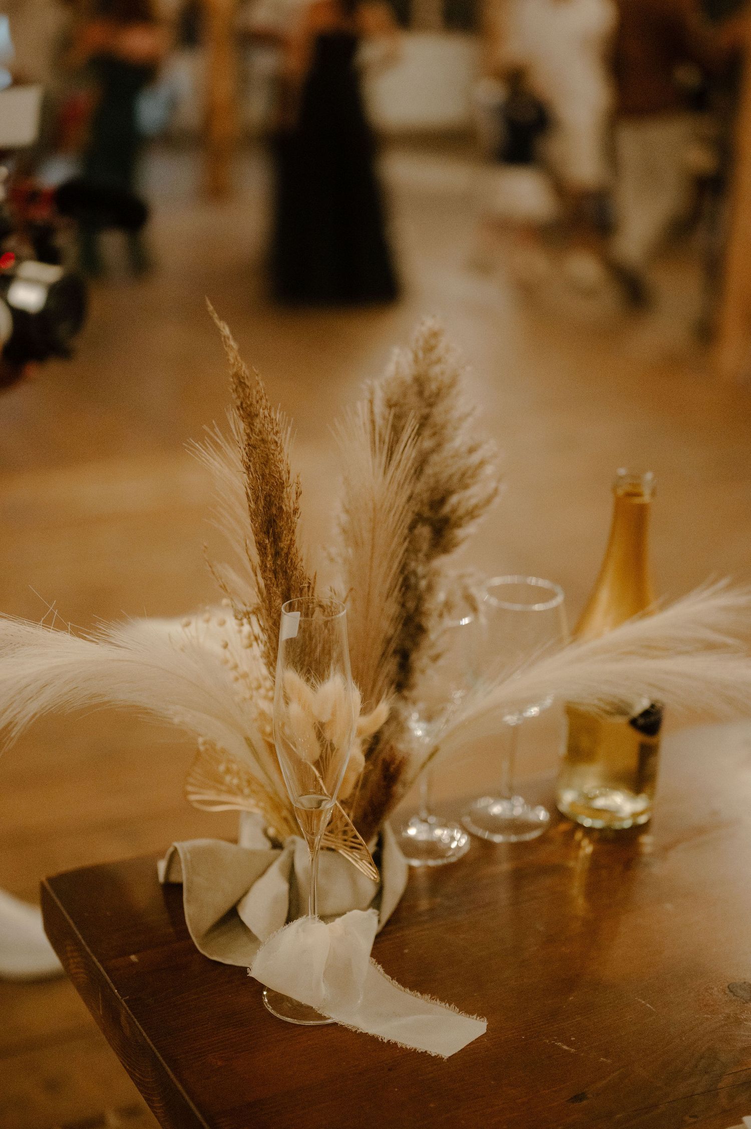 Wedding reception table centerpiece featuring dried pampas grass and white flowers in a minimalist arrangement.