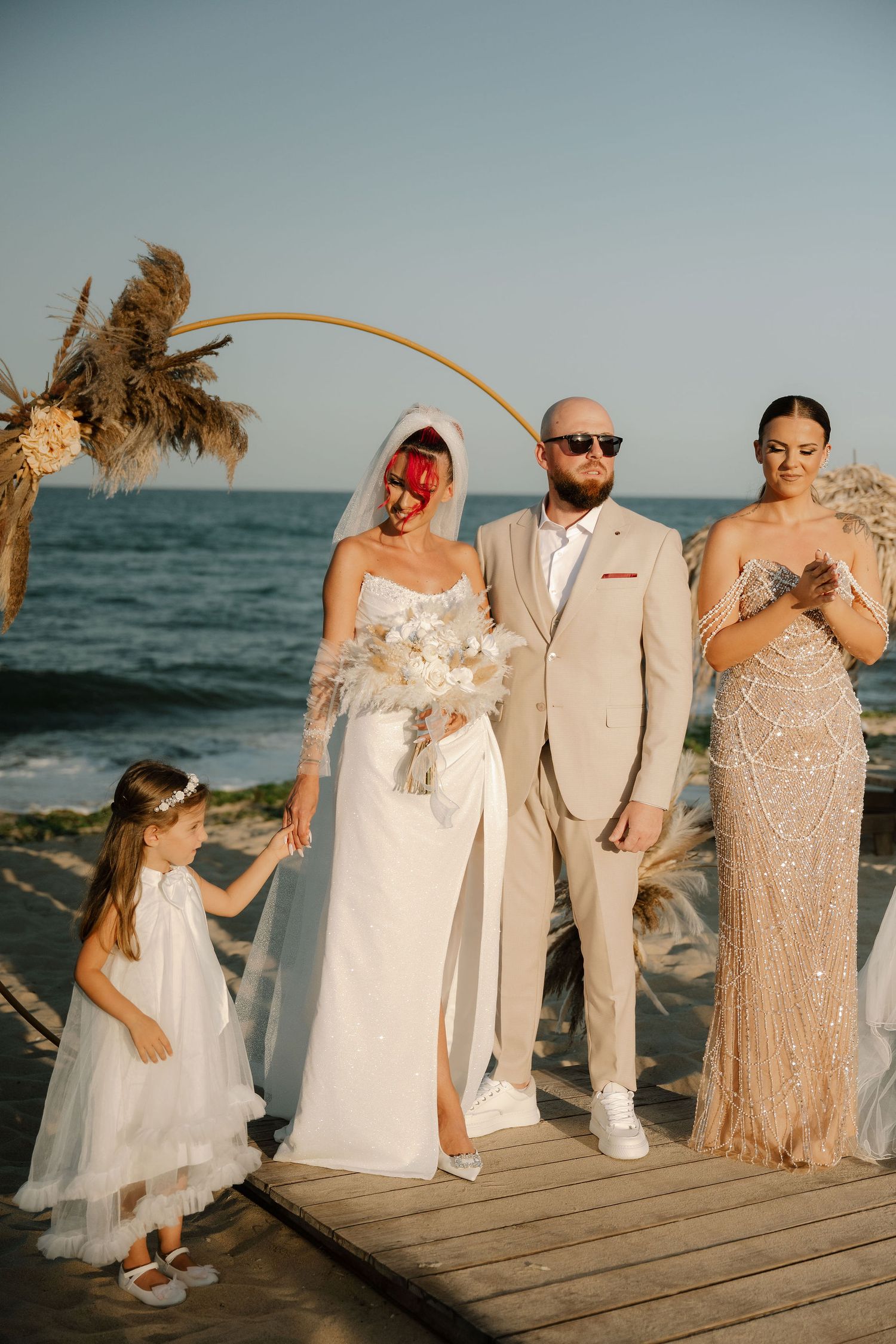 Wedding party poses on wooden boardwalk at sunset beach in coordinated white and beige formal attire.