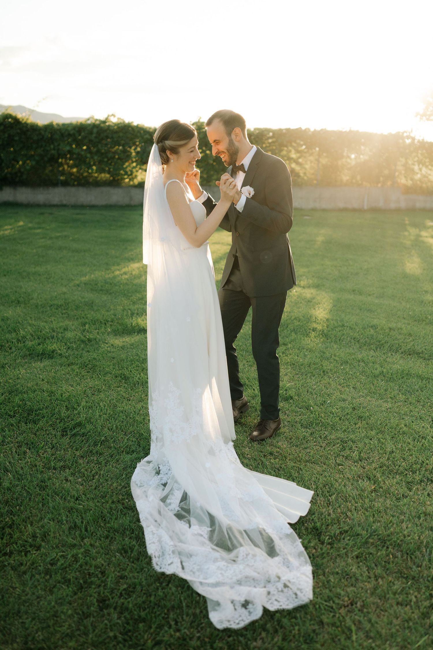 Newlyweds share an intimate dance on a grassy lawn during golden hour with her flowing white gown.