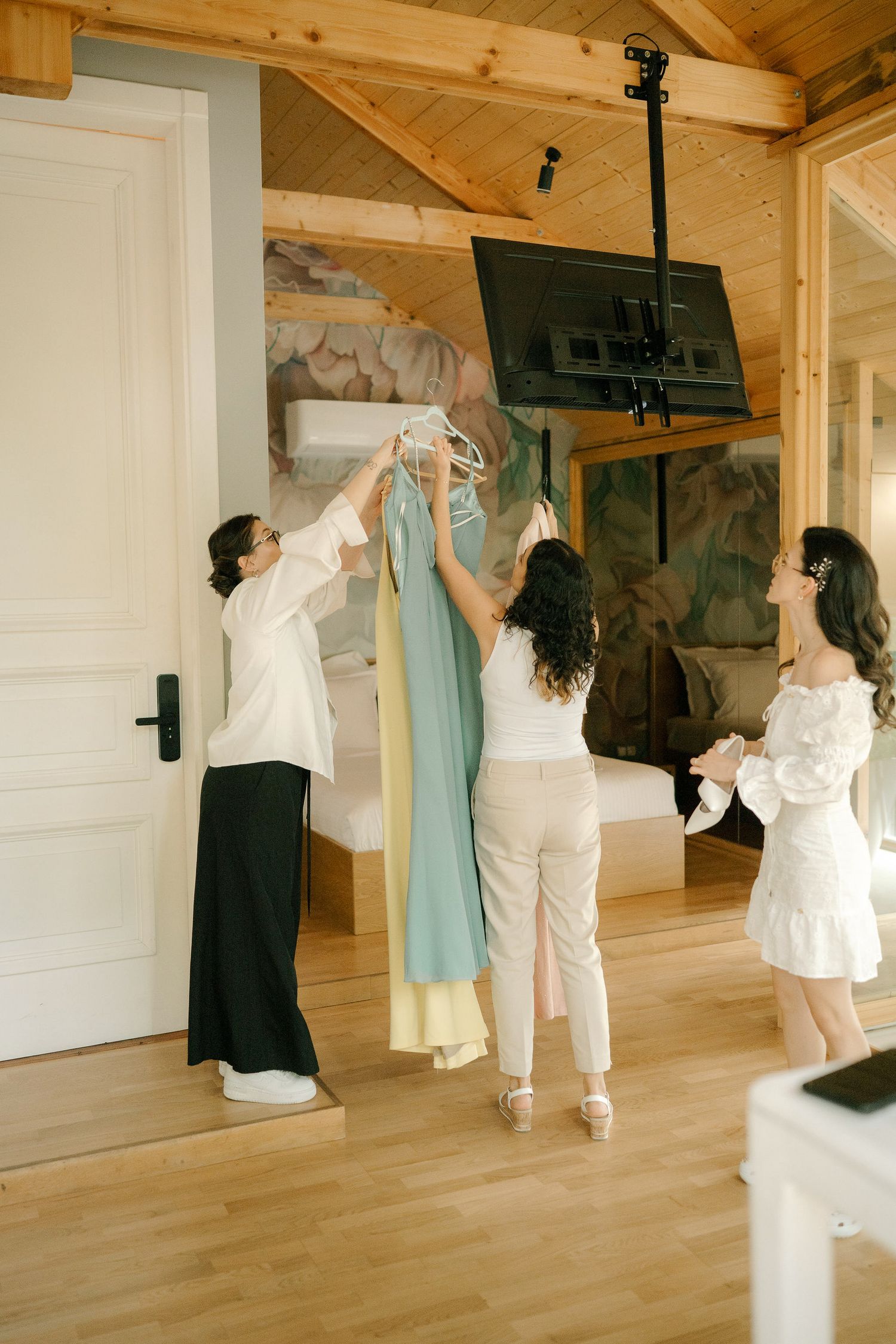 Multiple wedding dresses and formal attire displayed on hangers in a rustic wooden room with hardwood floors.