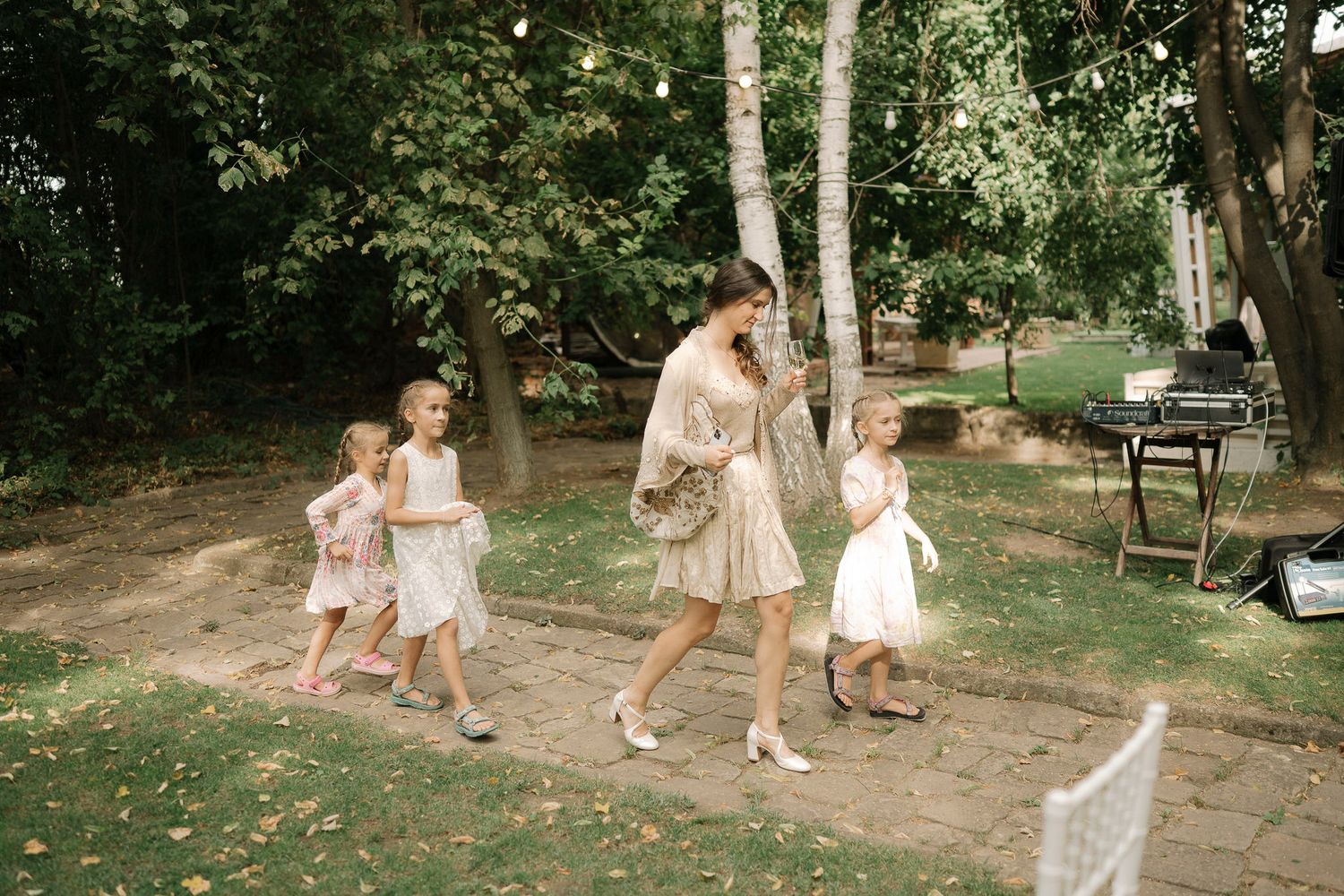 A group walks in line along a garden path surrounded by trees on a sunny summer afternoon.