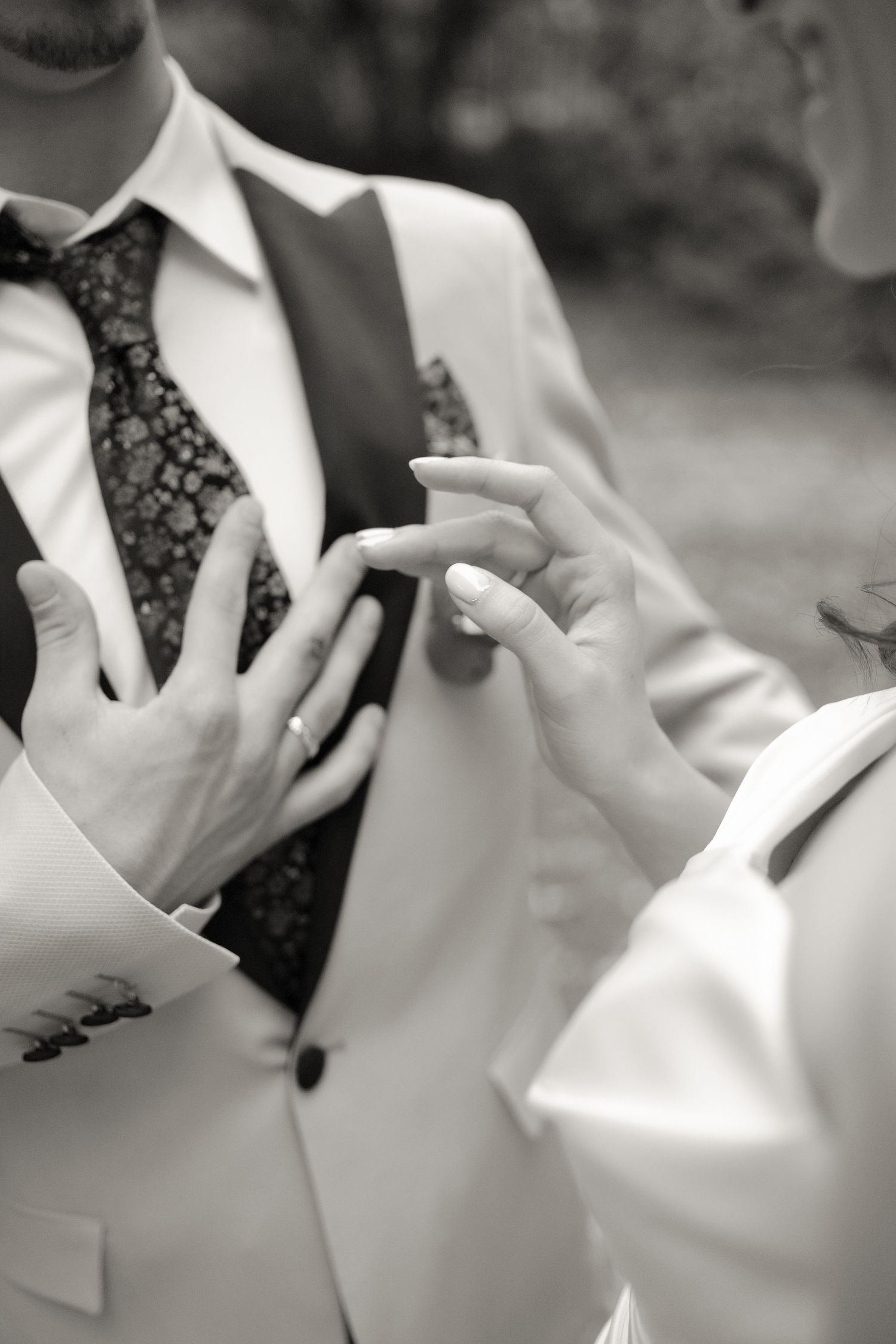 Close-up black and white image showing hands adjusting a formal tie and suit vest.