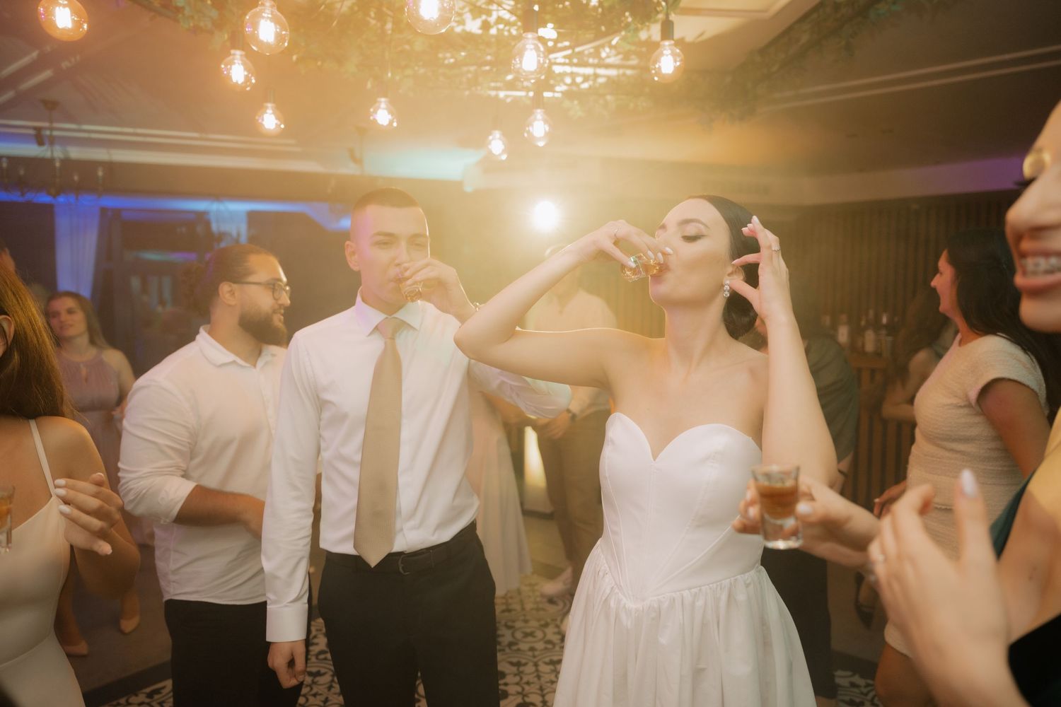 A couple celebrates on the dance floor at their wedding reception under glowing pendant lights.