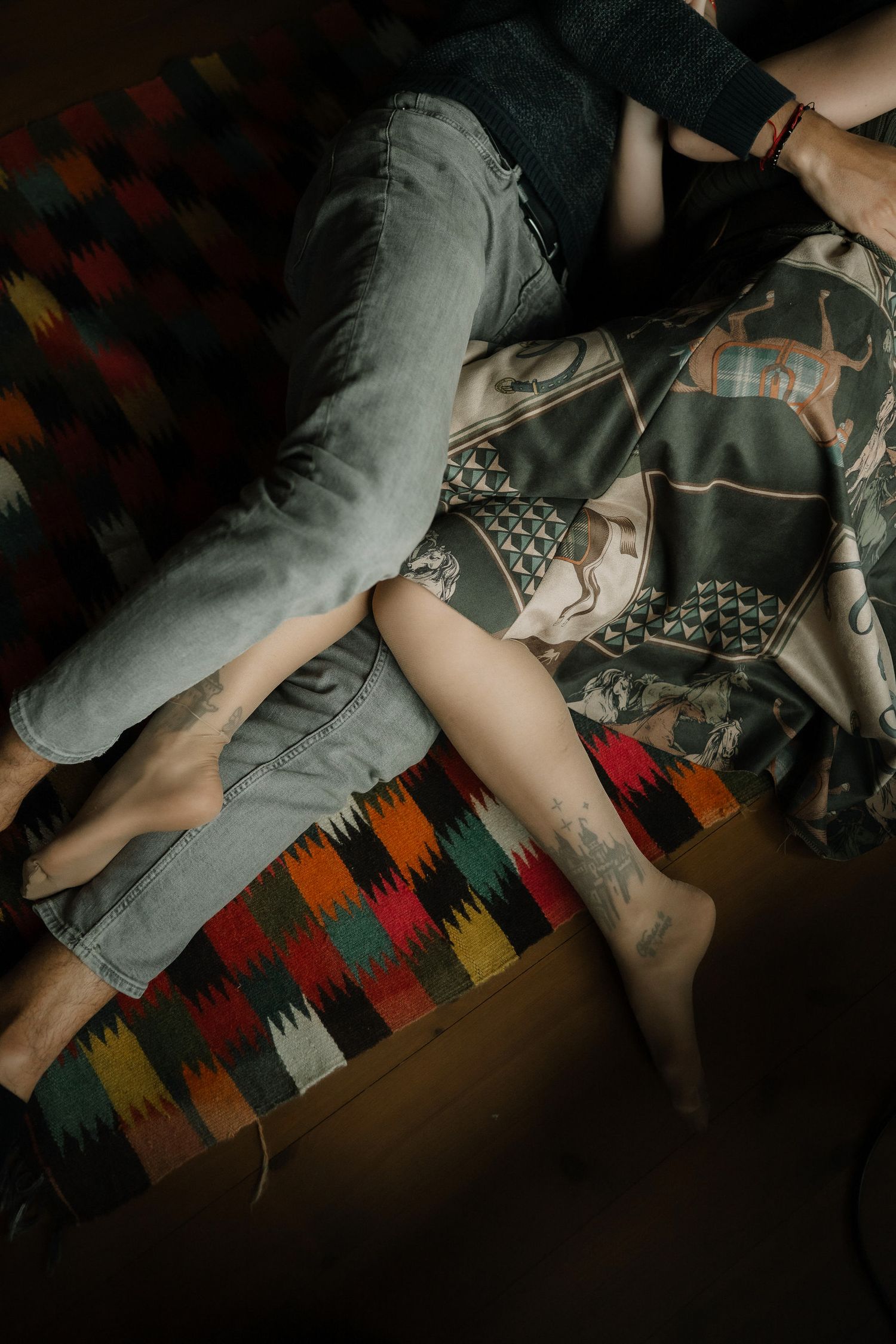 A person lies on a colorful geometric patterned blanket in a dimly lit room.