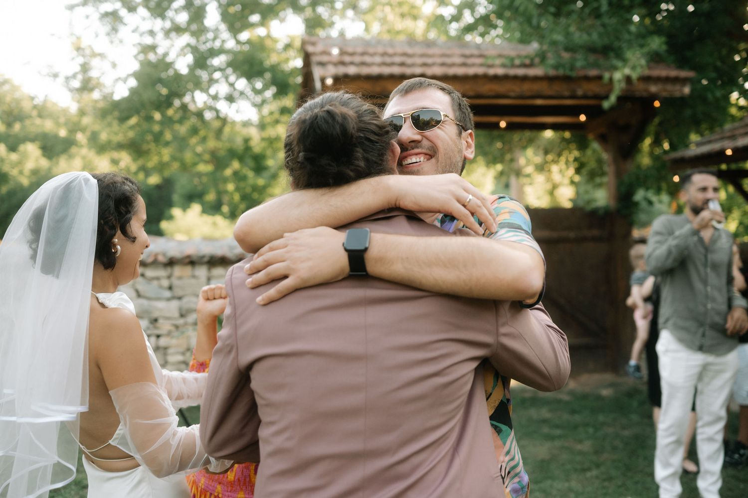 A joyful embrace between wedding guests takes place during an outdoor garden celebration.