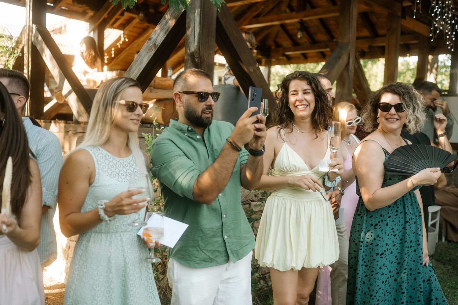 Wedding guests in green and white attire mingle and celebrate at an outdoor reception venue.