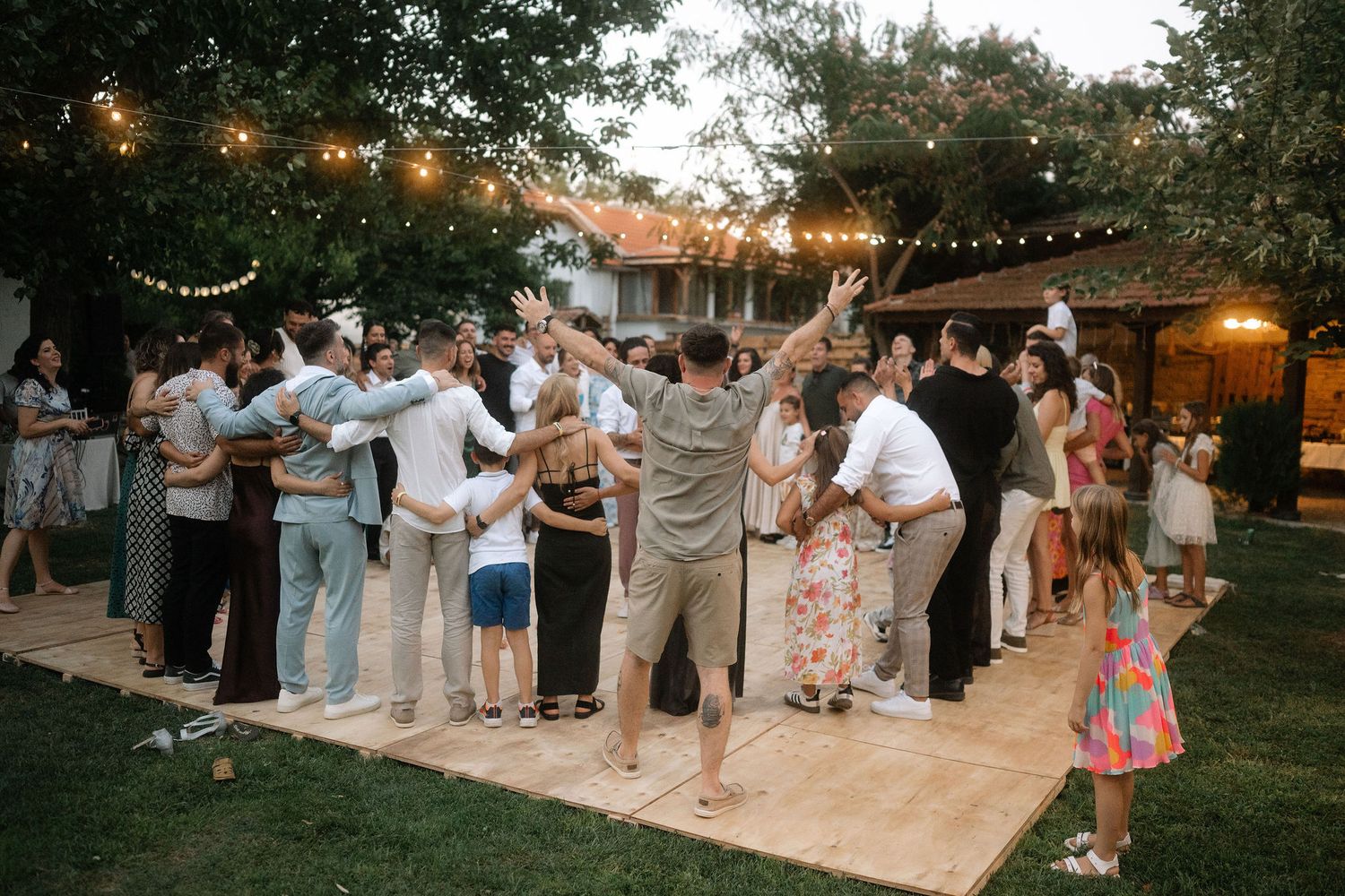 Wedding guests dance together on an outdoor patio decorated with string lights during an evening reception celebration.