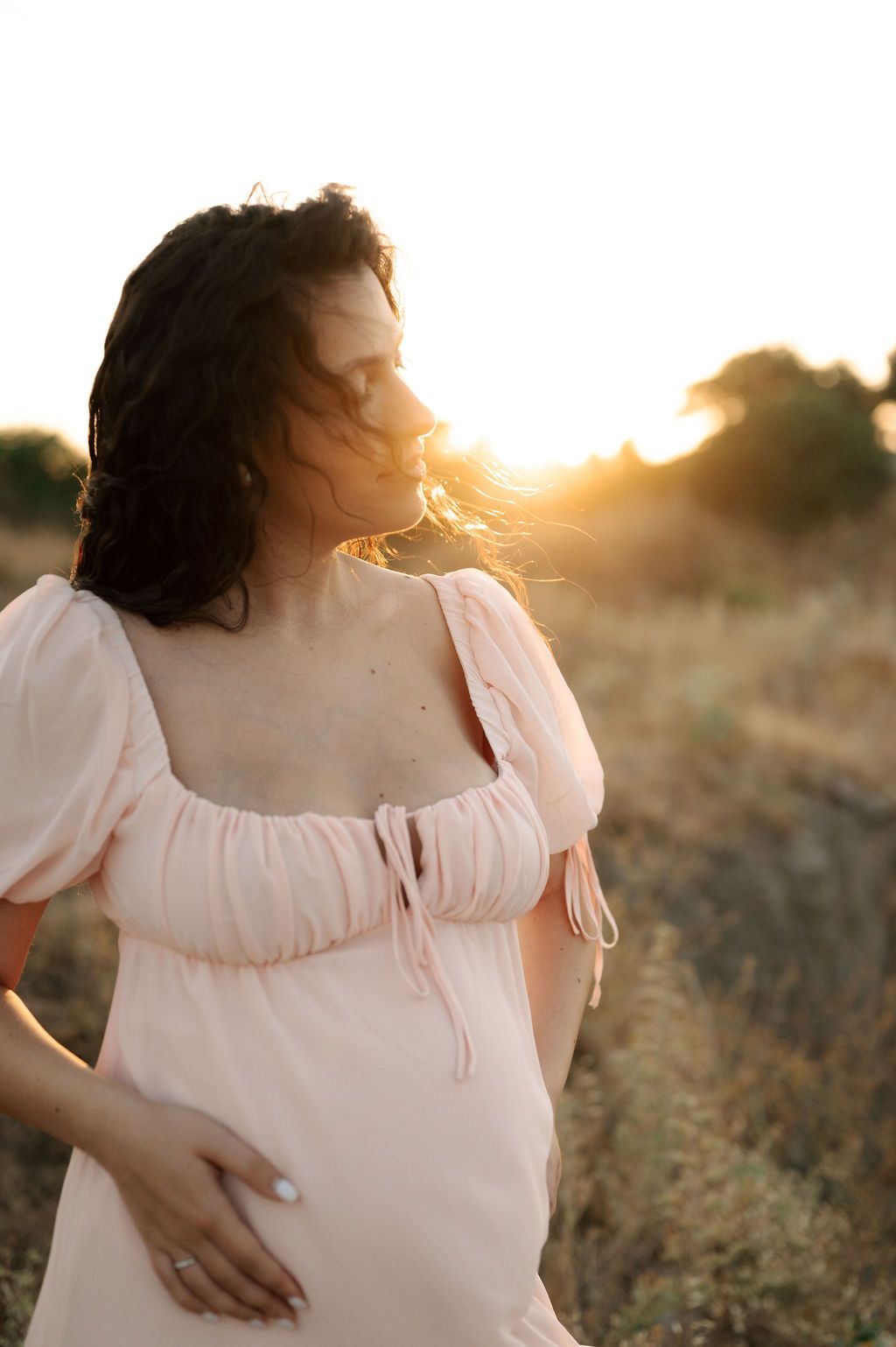A person in a white dress poses in a golden field at sunset, creating a dreamy and romantic atmosphere.