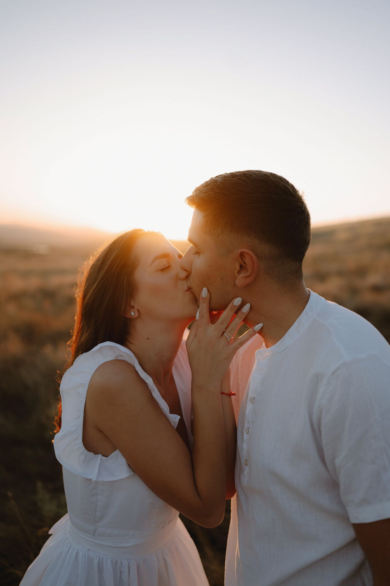 A couple shares tender kisses at sunset against a golden desert landscape backdrop.