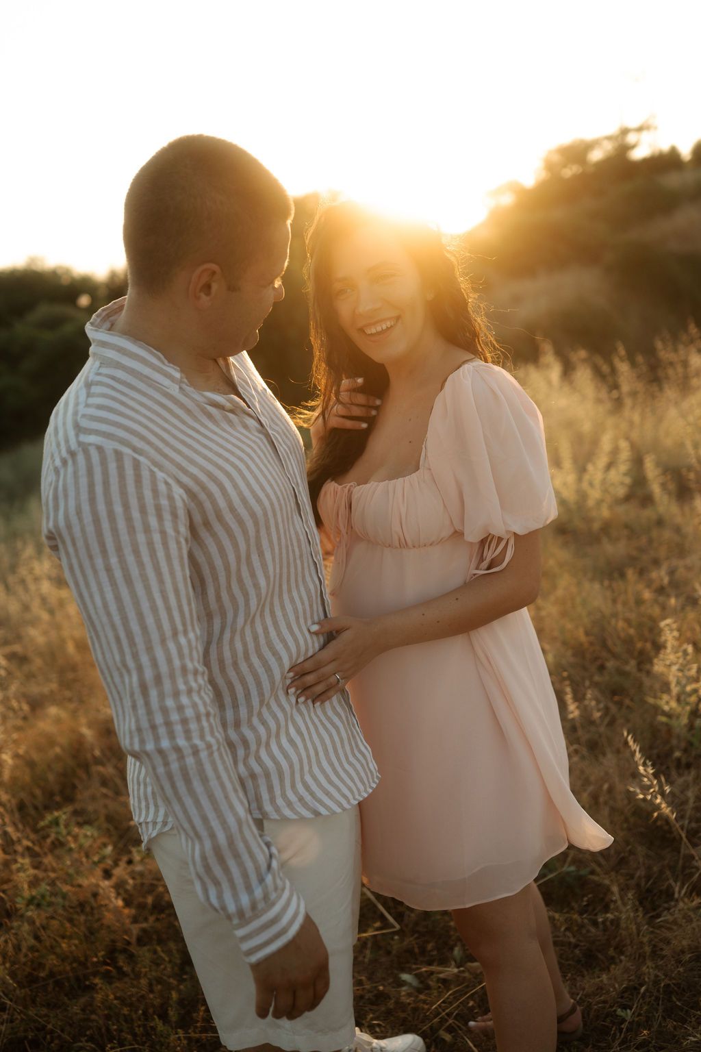 A romantic maternity photoshoot in a field at golden hour with soft sunlight creating a dreamy atmosphere.