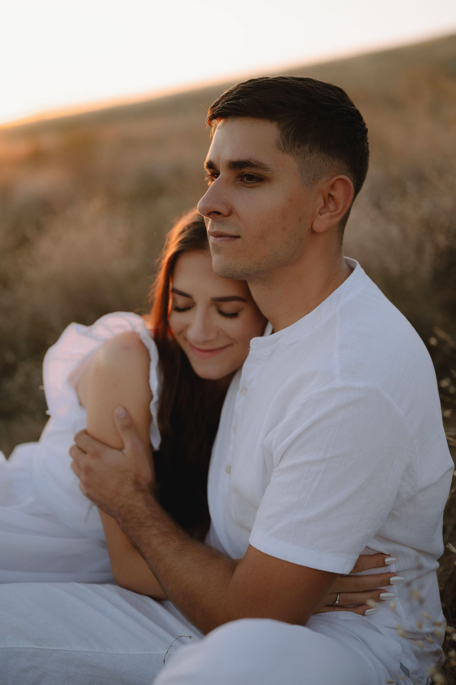 Romantic couple embraces during golden hour photoshoot in matching white outfits.